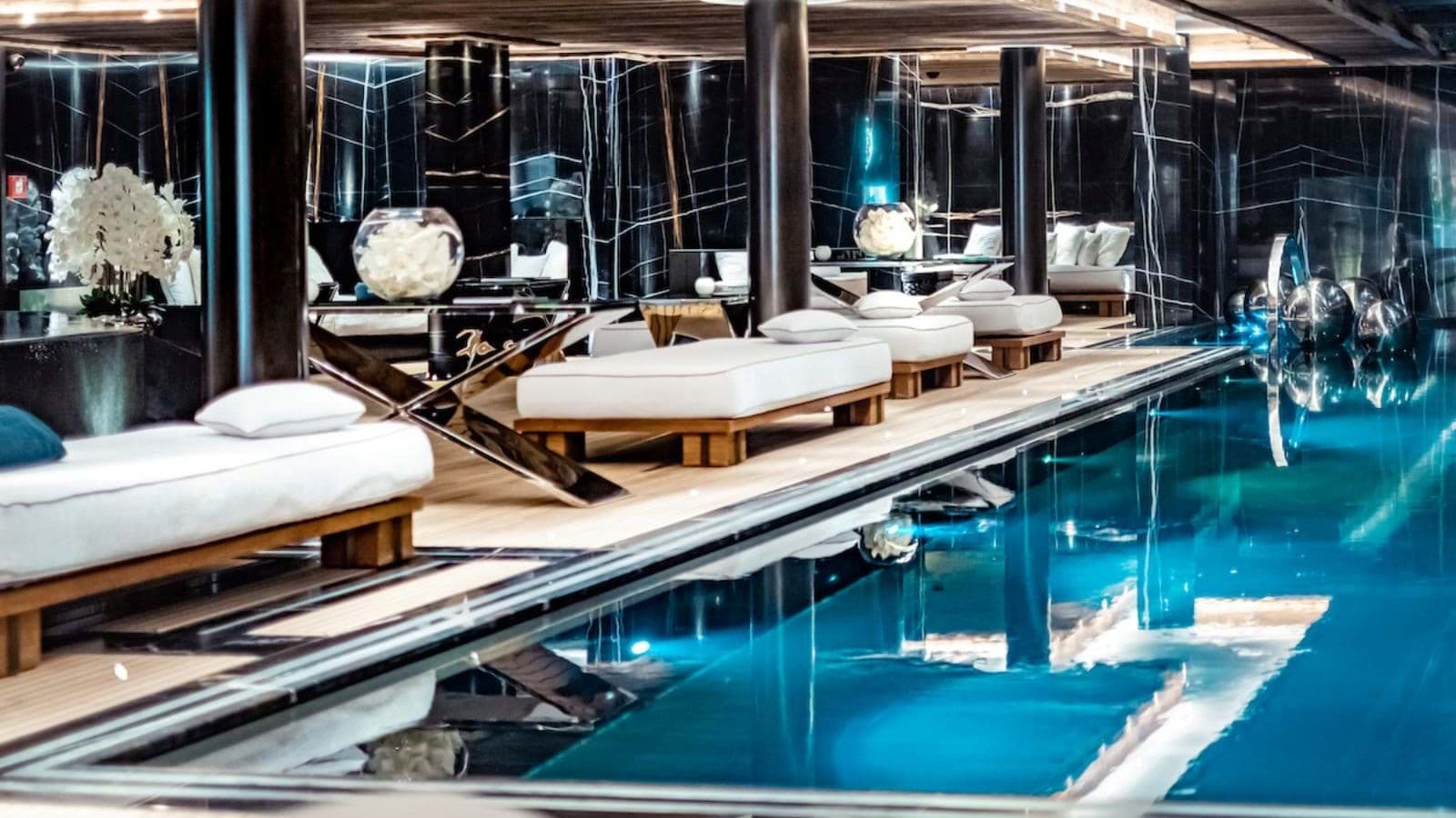 Indoor lap pool with poolside daybeds and black marble walls