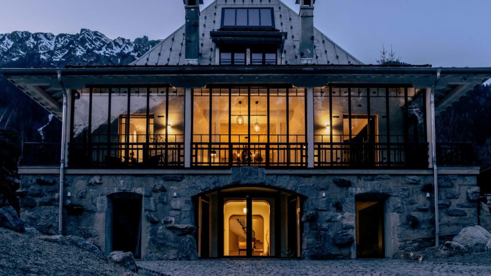 Stone and glass chalet facade with floor-to-ceiling windows and mountain backdrop