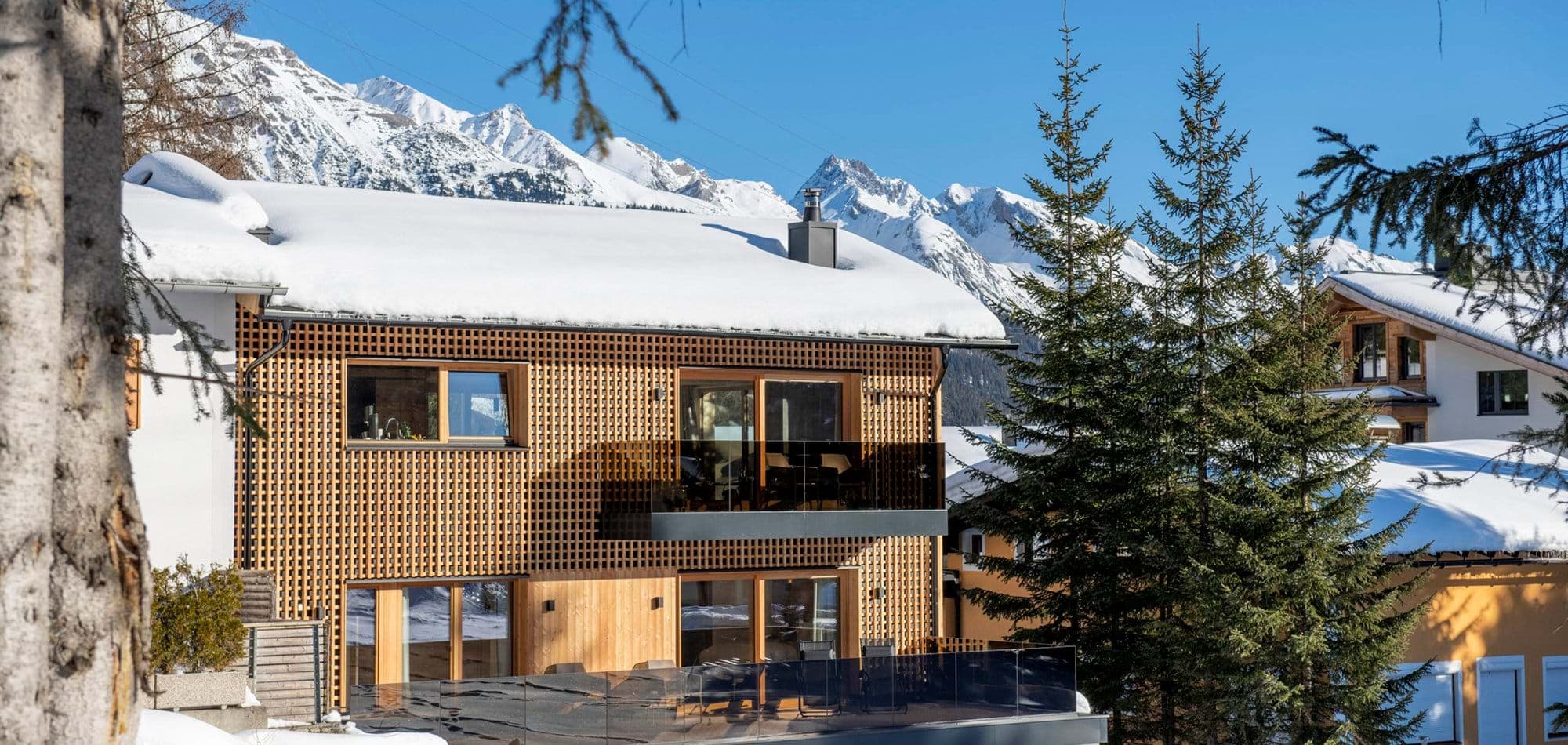 Chalet exterior with timber cladding and glass-fronted balconies facing mountain peaks