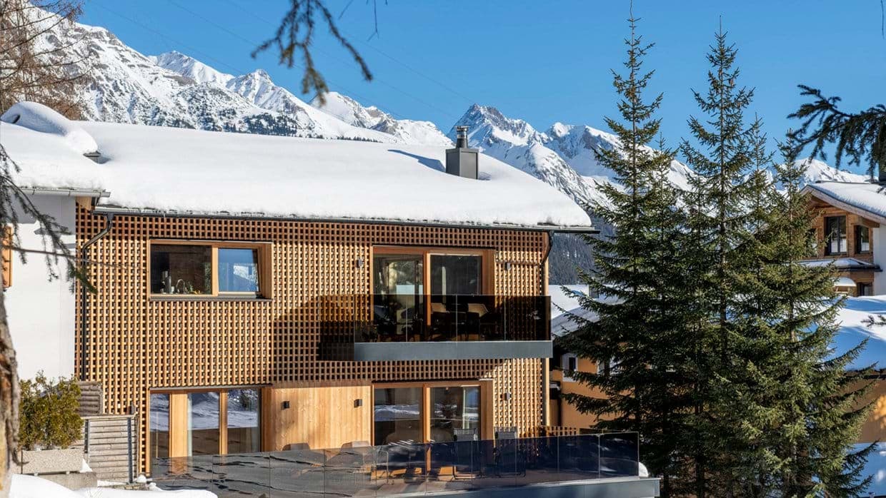 Chalet exterior with timber cladding and glass-railed balconies facing the Alps