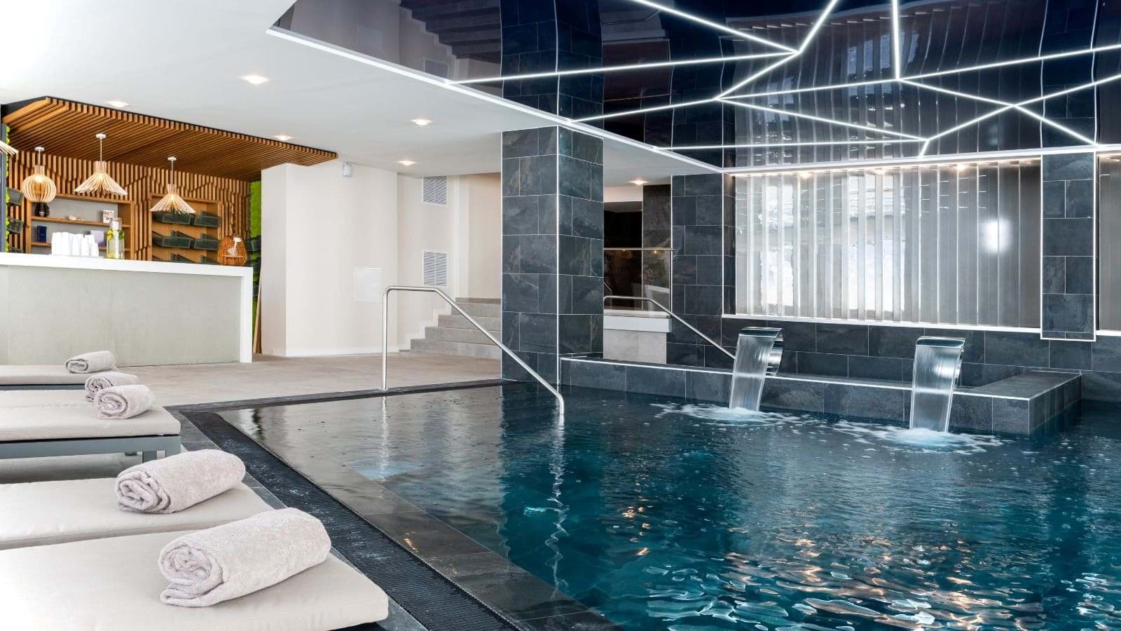 Indoor pool with dual waterfall features and heated lounging deck