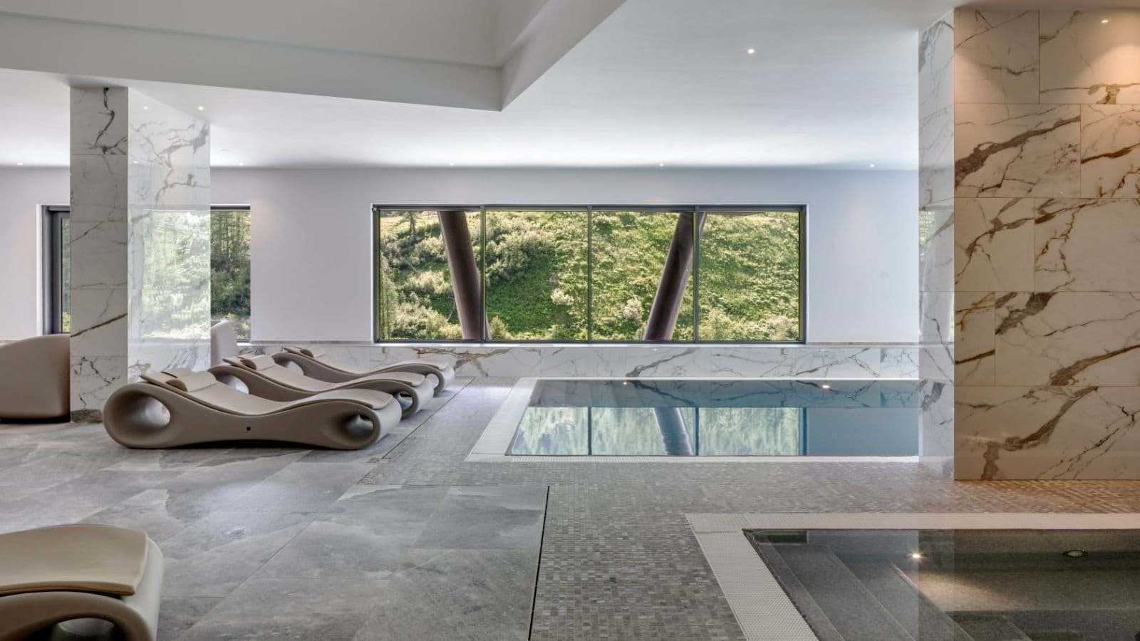 Indoor pool and hot tub with curved loungers and hillside views