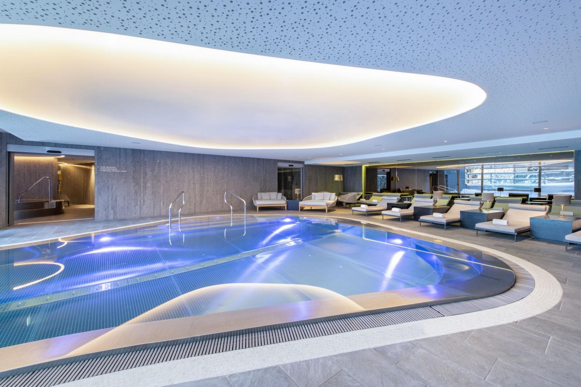 Indoor heated pool with poolside lounge seating and acoustic ceiling