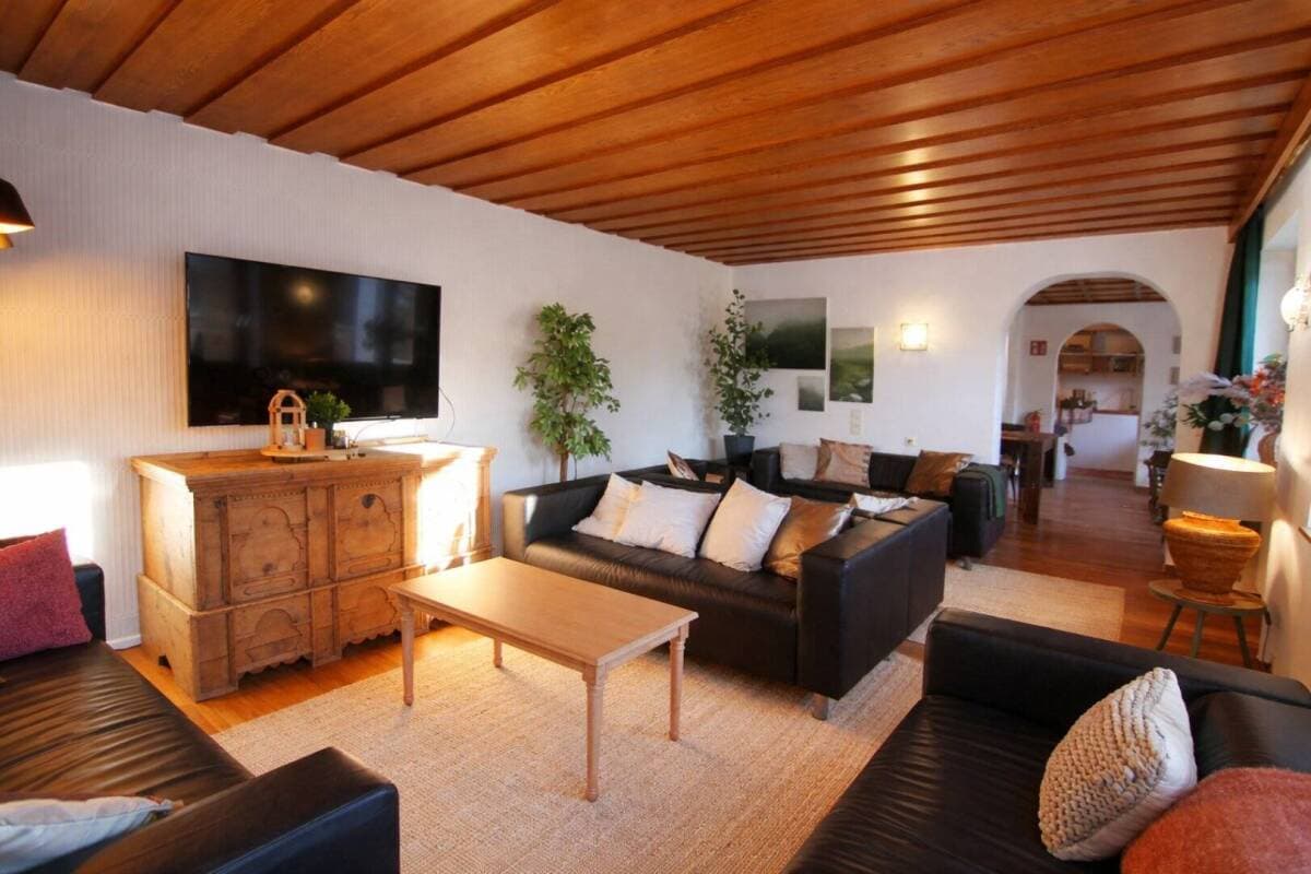Open-plan living room with black sectional, wood ceiling, and TV above wooden sideboard