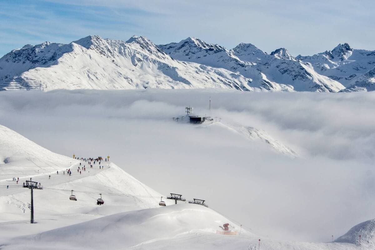 Ski resort view above clouds with lift access and mountain peaks