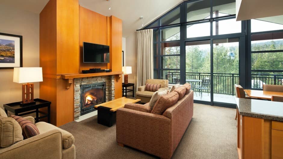 Living area with stone fireplace and floor-to-ceiling forest views