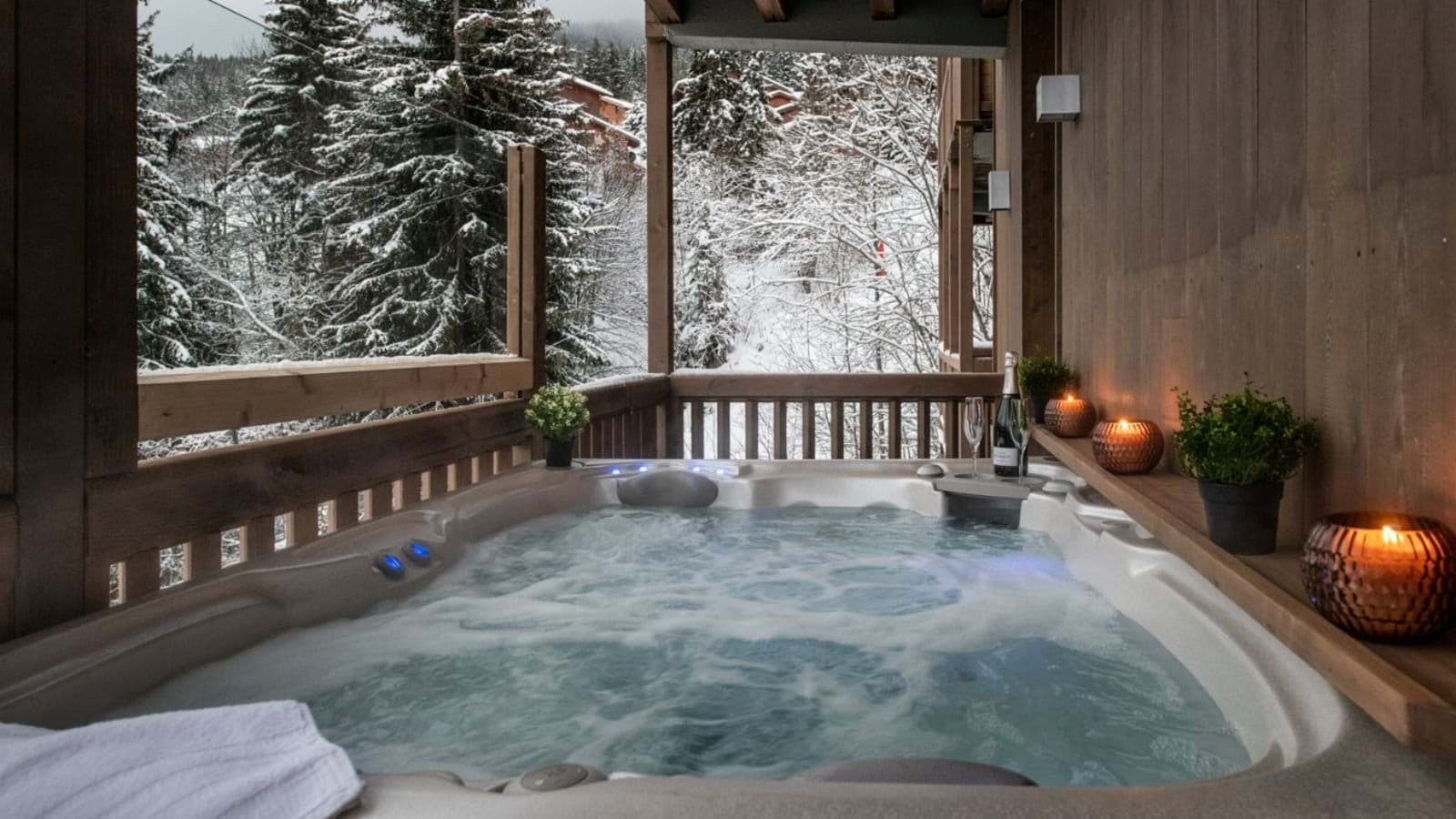 Covered outdoor hot tub with snowy forest view and integrated lighting