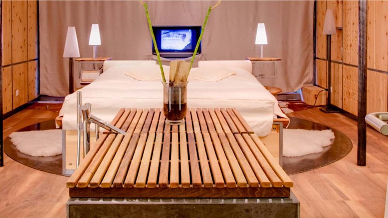 Open-concept bedroom with king bed and in-room bathtub featuring slatted wood cover