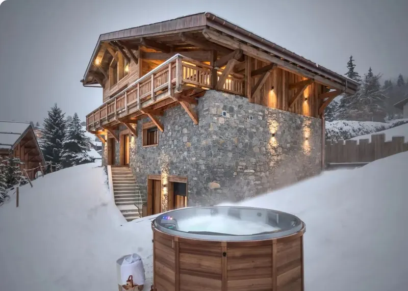 Stone and timber chalet at dusk with a steaming hot tub in the snow