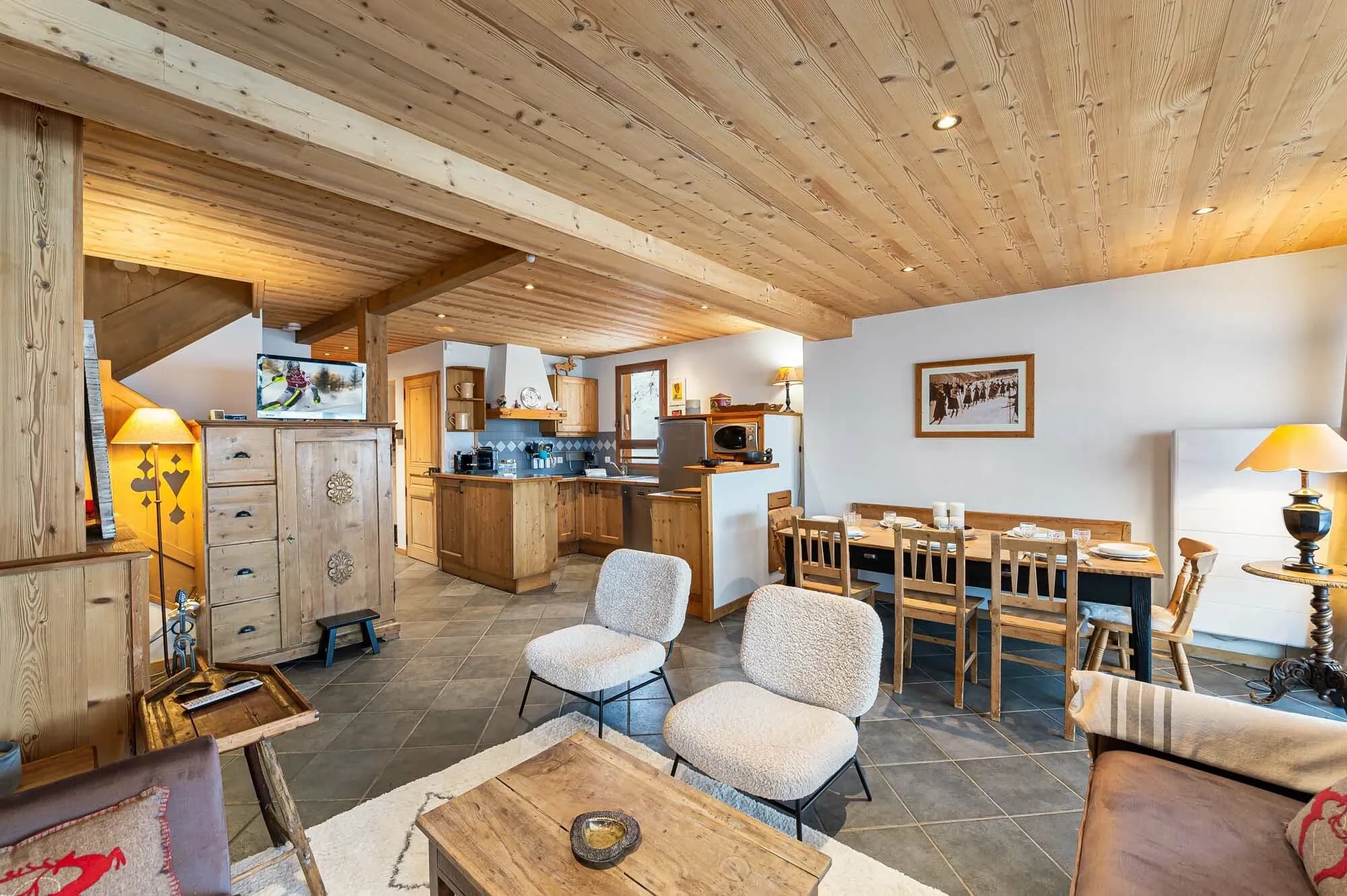 Open-plan lounge and dining area with kitchen behind, wood ceiling and slate floor