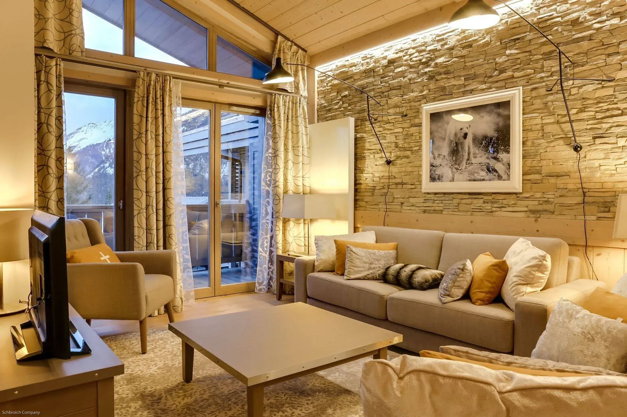 Living room with stone feature wall, sofa, armchair and glass doors to balcony