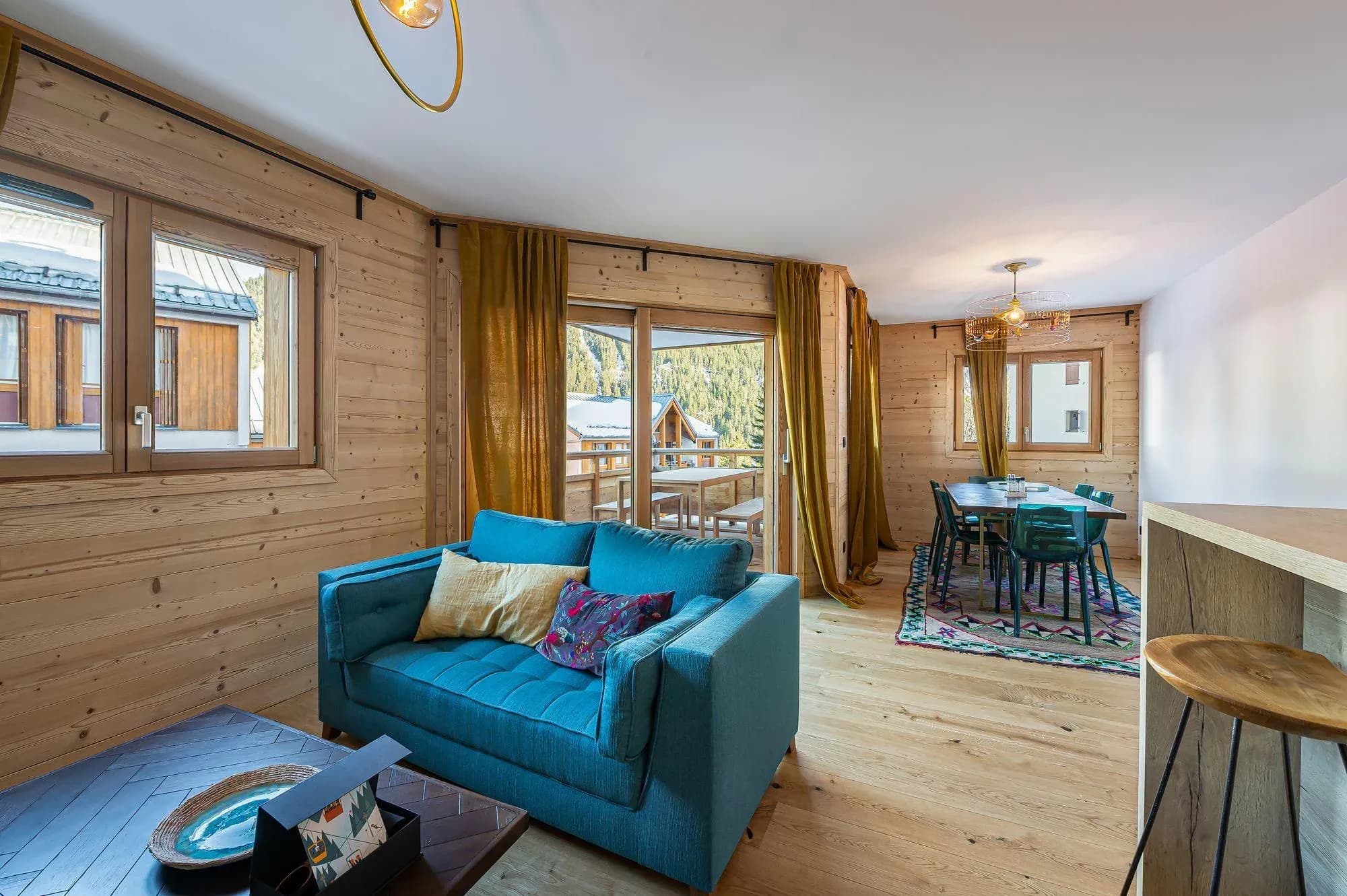 Living room with teal sofa, wood-clad walls and balcony access