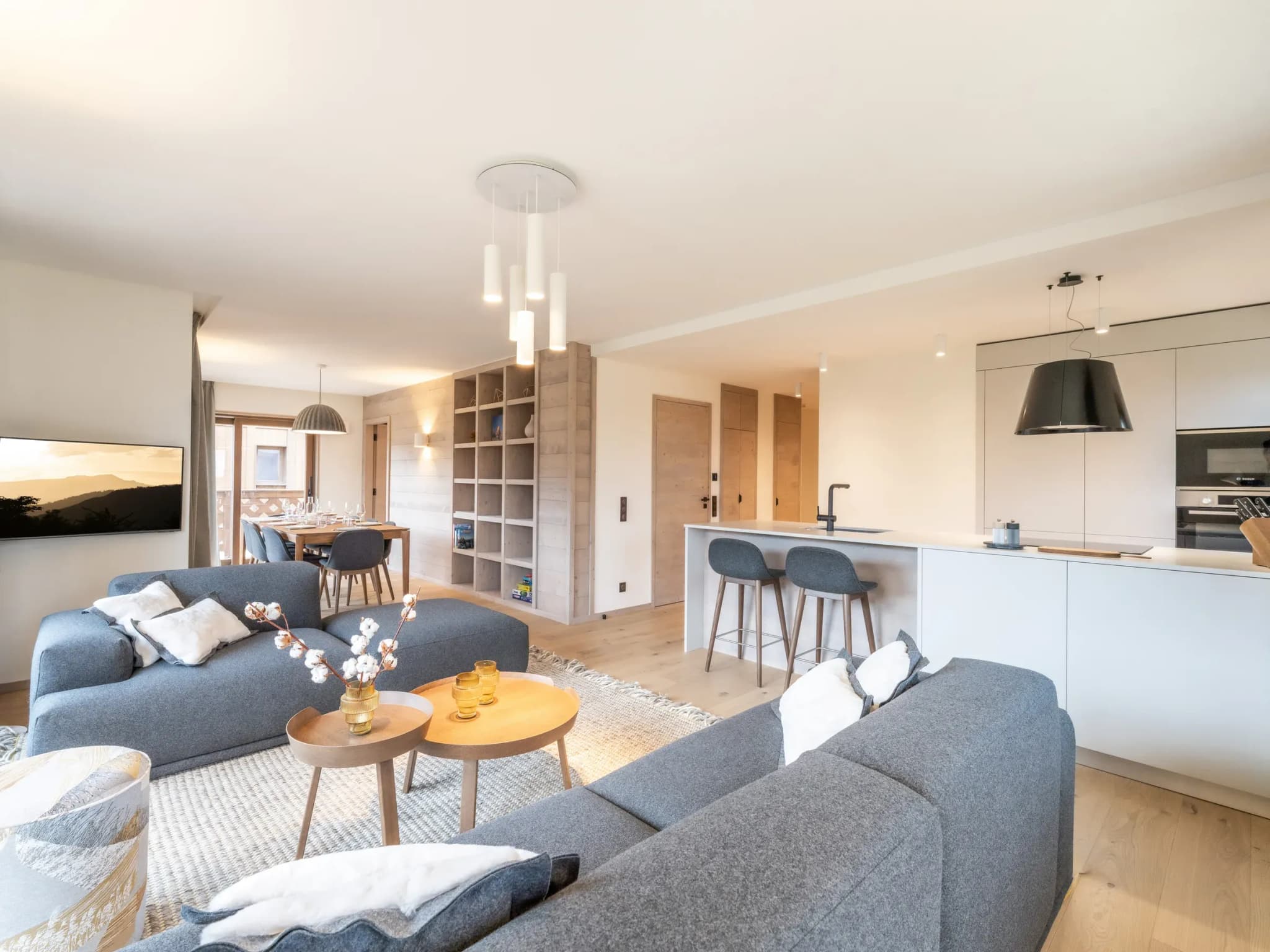 Open-plan living room with grey sofas, wooden coffee tables and kitchen breakfast bar with two stools