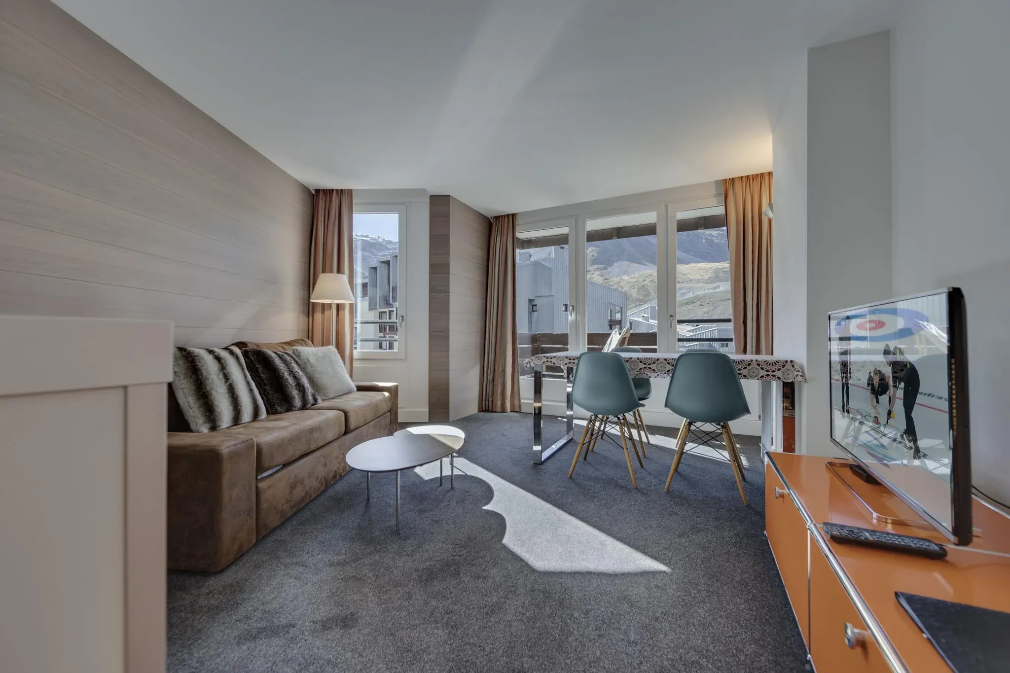 Living room with sofa, coffee table, TV and balcony doors facing the mountains