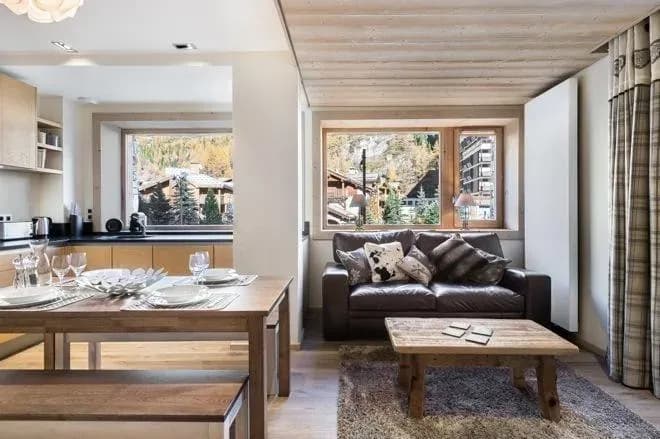 Open-plan lounge with brown leather sofa, wooden coffee table and dining table beside the kitchen