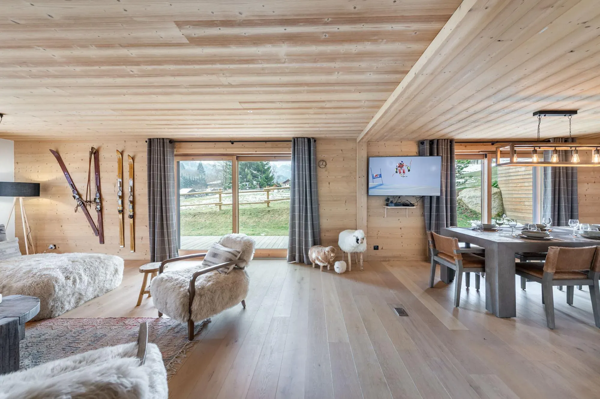 Open-plan living room with sheepskin armchairs, vintage skis on the wall and sliding doors to the terrace