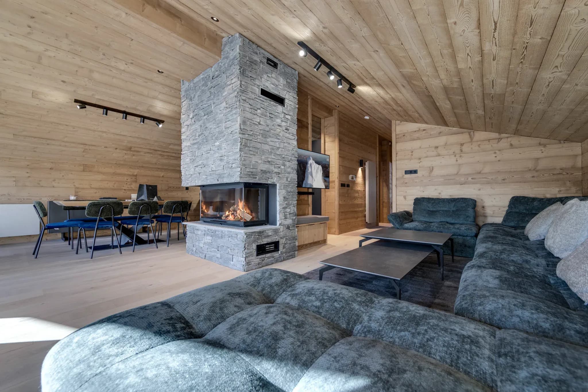 Living area with central stone fireplace, grey corner sofa and dining table behind