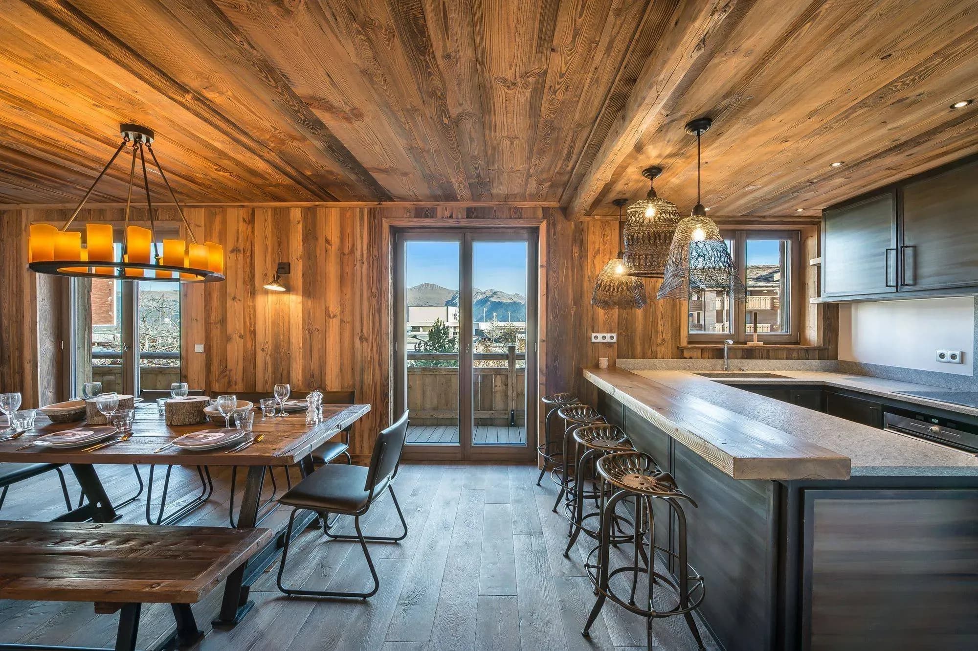 Open kitchen and dining area with bar stools, wooden table, bench and balcony door