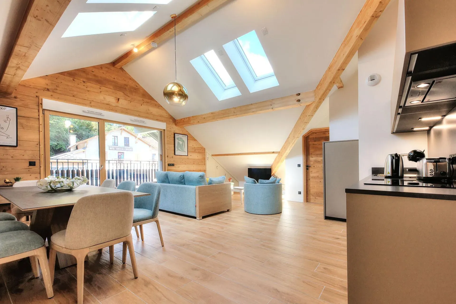 Open-plan living area with dining table, blue sofa and skylights under exposed beams