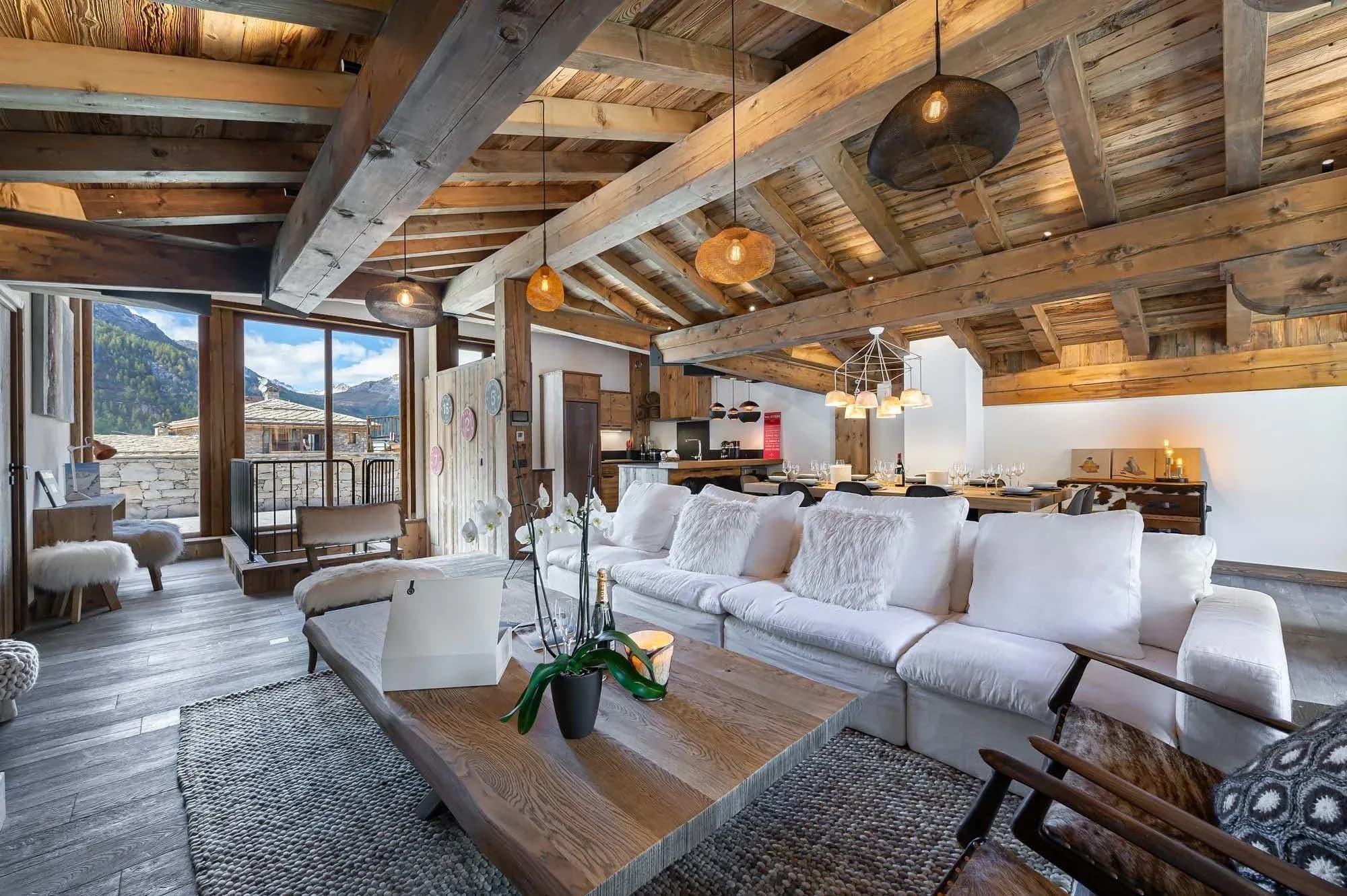 Open-plan lounge with white corner sofa, exposed beams and mountain view