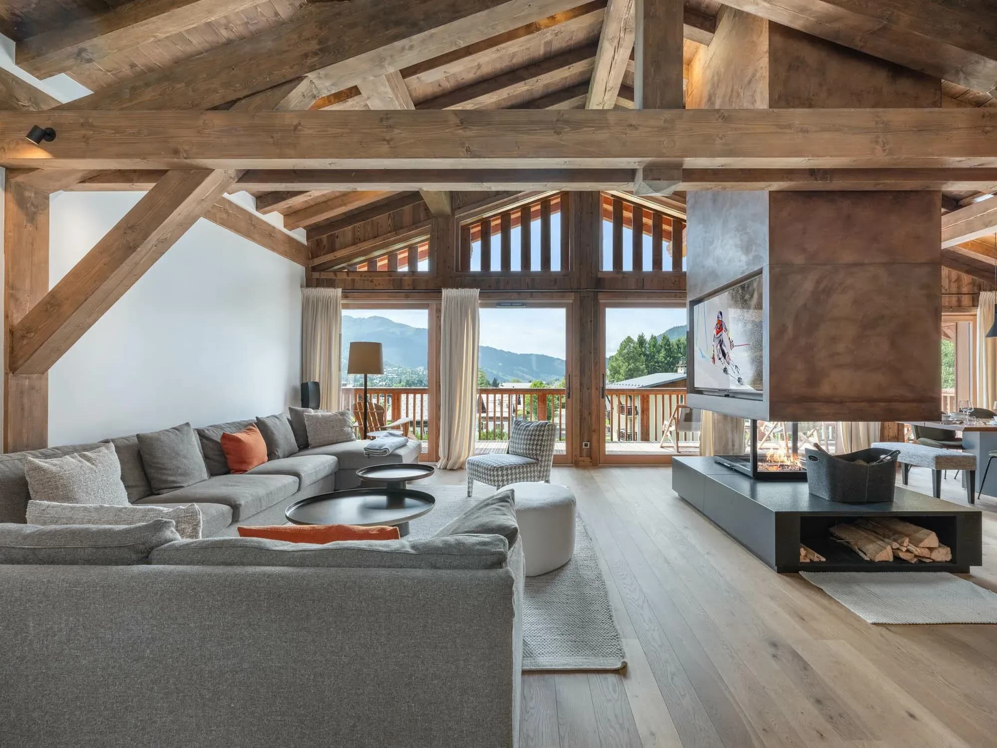 Living room with grey corner sofa and central fireplace facing mountain views