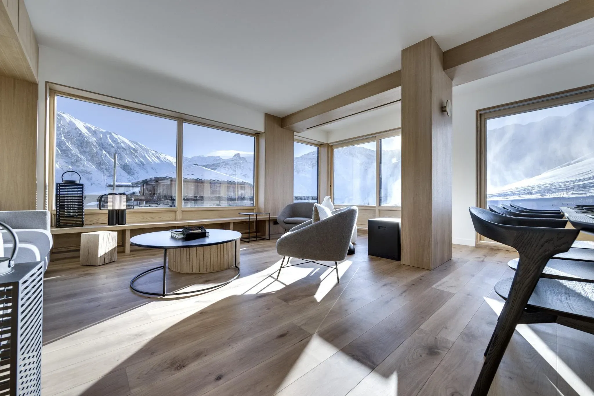 Living area with round coffee table, armchairs and corner windows onto snowy slopes