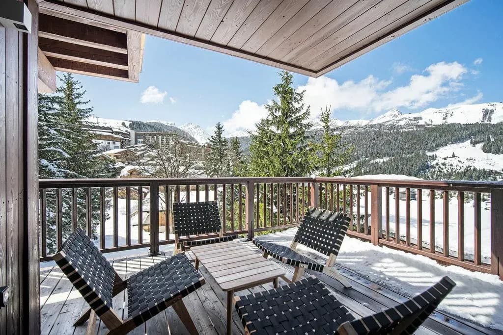 Covered balcony with four woven chairs, low table and snowy mountain view