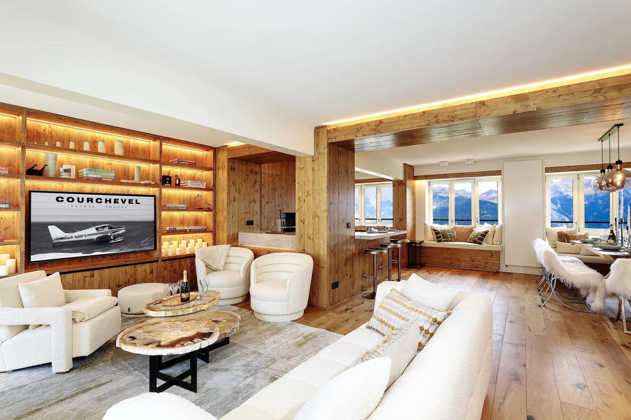 Living room with white sofas, wall-mounted TV in wooden shelving and mountain-view windows