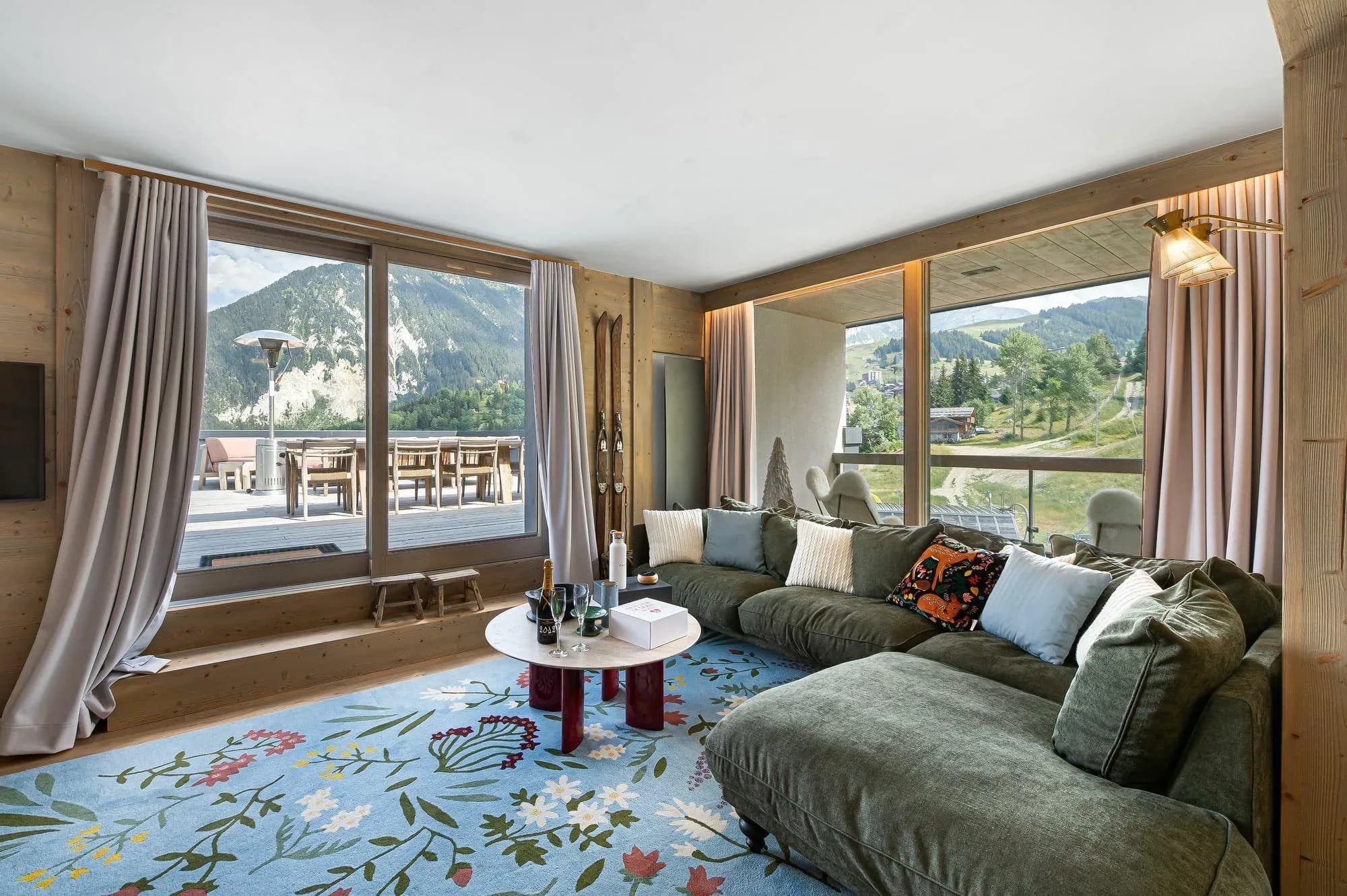 Living room with green corner sofa, floral rug and terrace doors facing the mountains