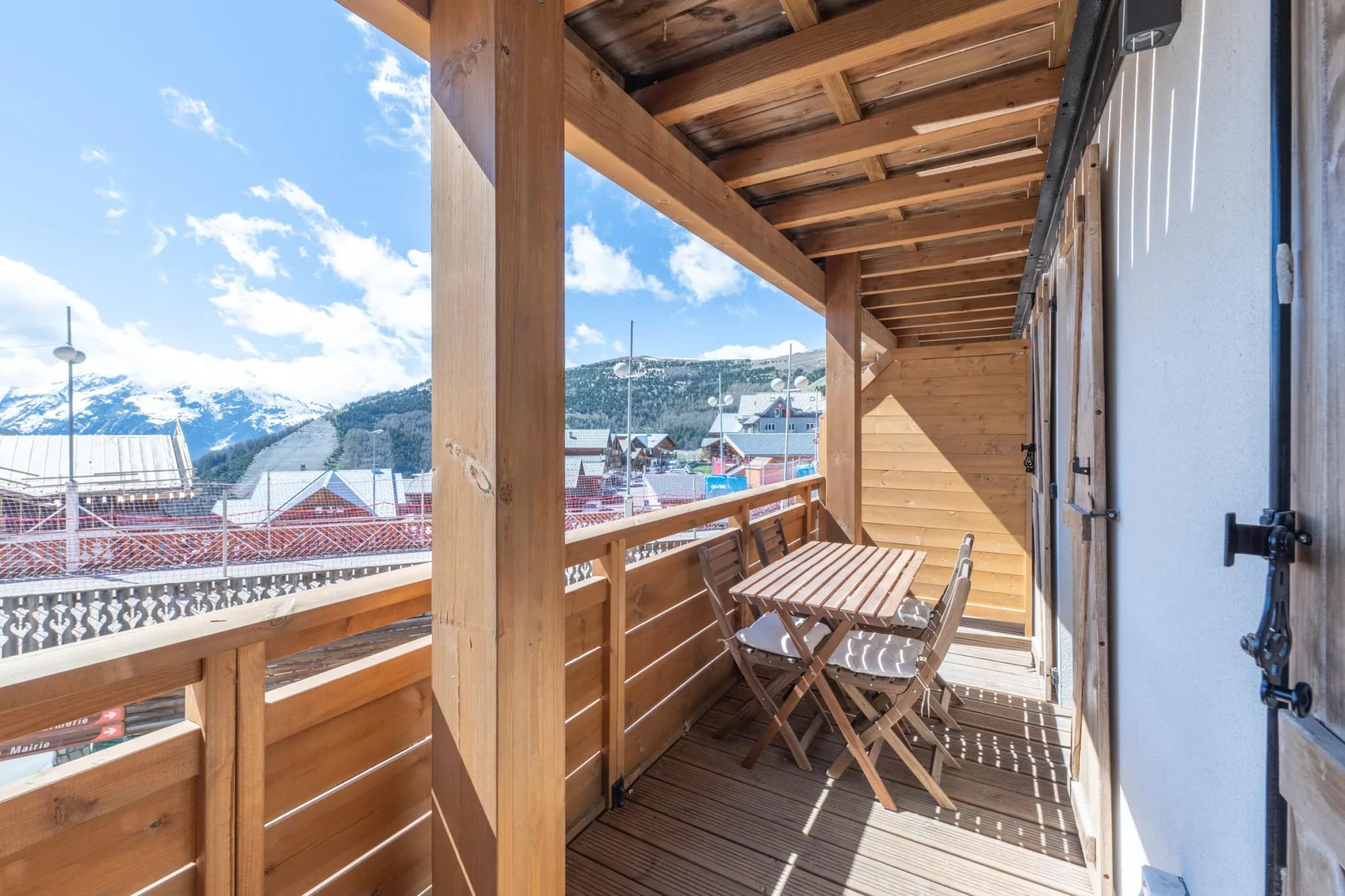 Covered wooden balcony with folding table and two chairs facing the mountains