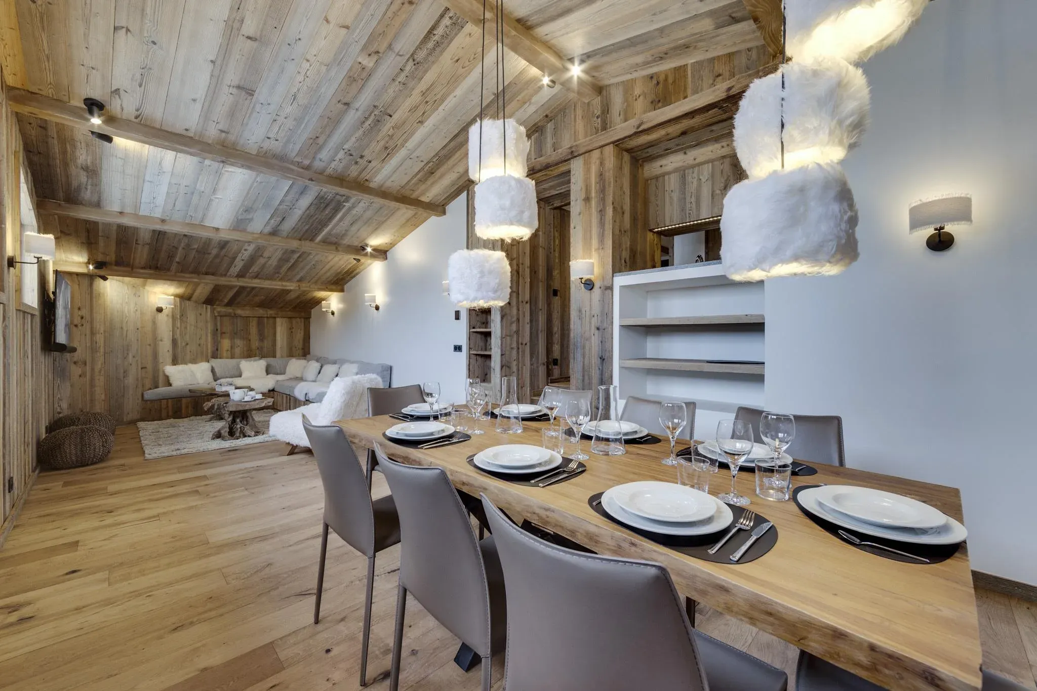 Dining table with grey leather chairs and fur pendant lights, lounge beyond
