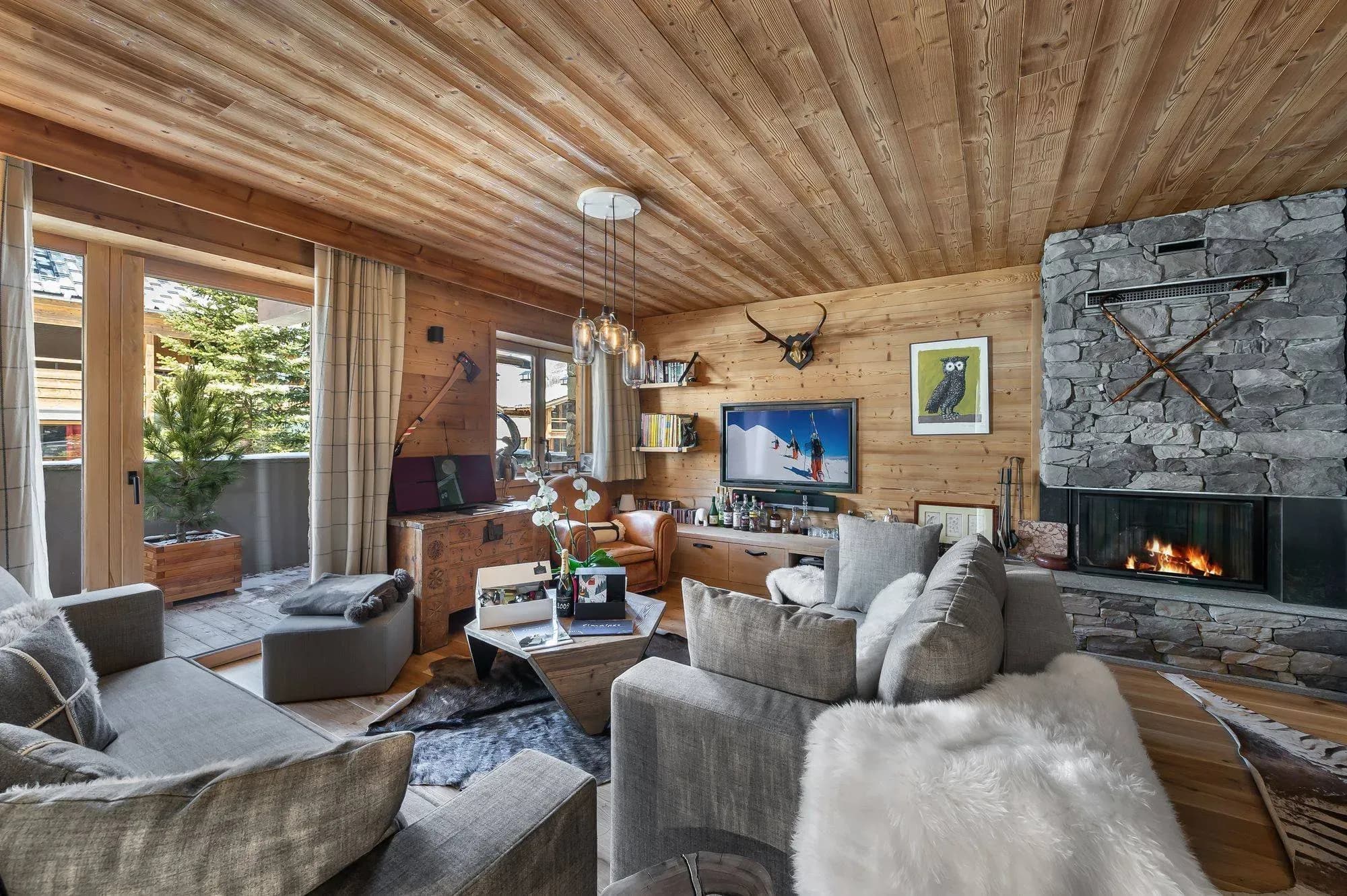 Living room with stone fireplace, grey sofas and wood-clad walls