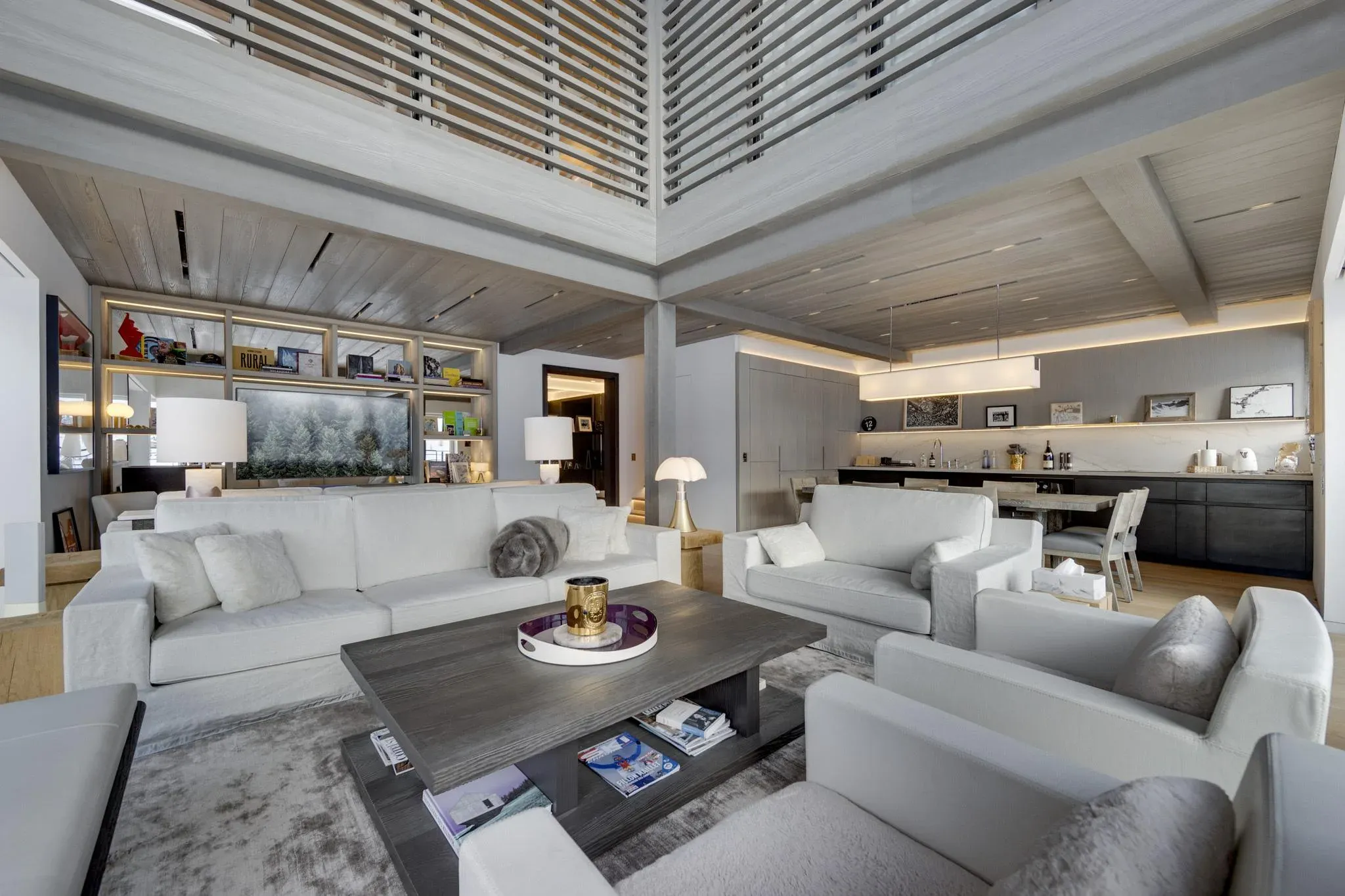 Double-height living room with white sofas, armchairs, wood coffee table and open kitchen behind