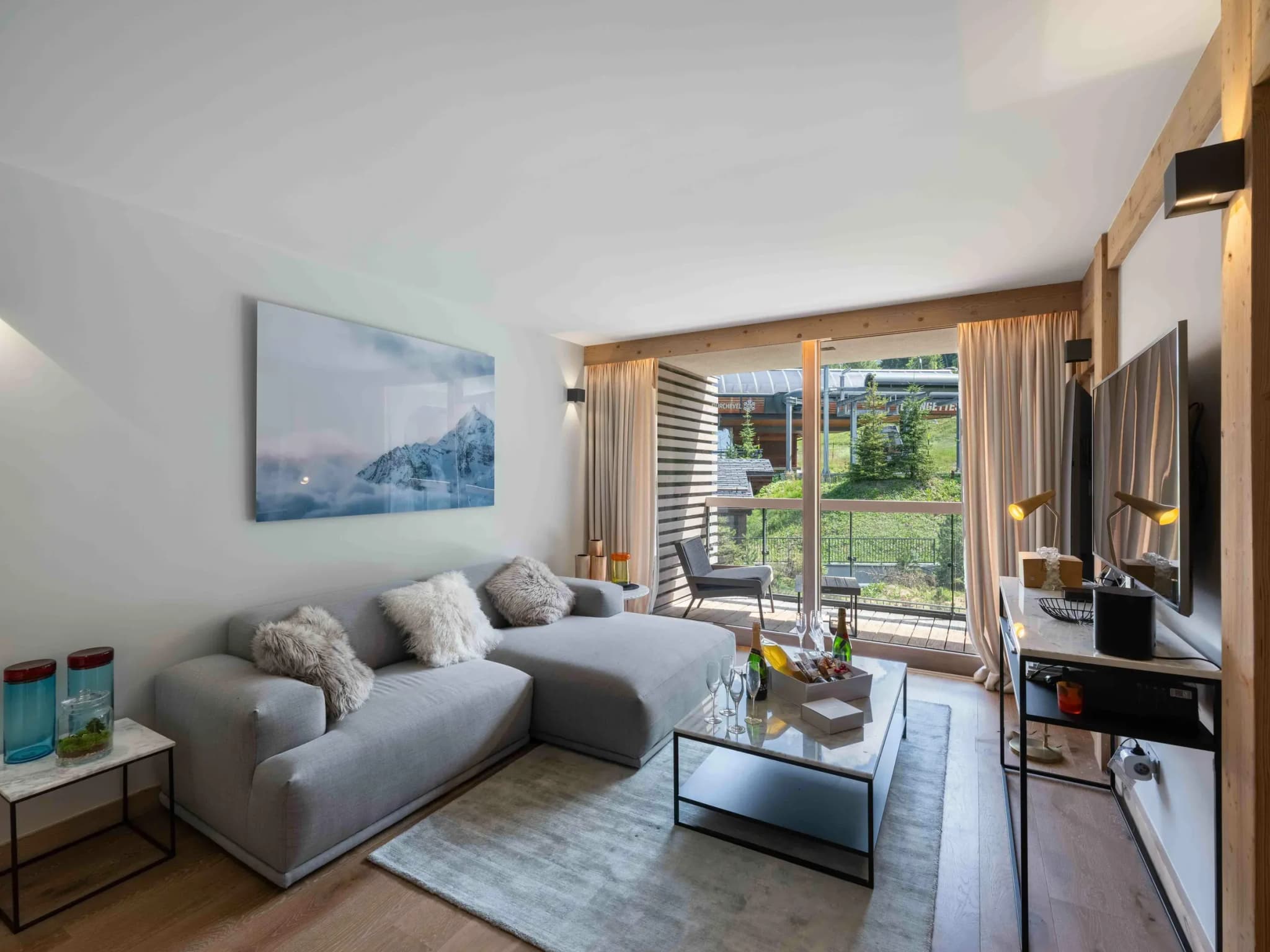 Living room with grey corner sofa, TV and balcony doors to the slopes