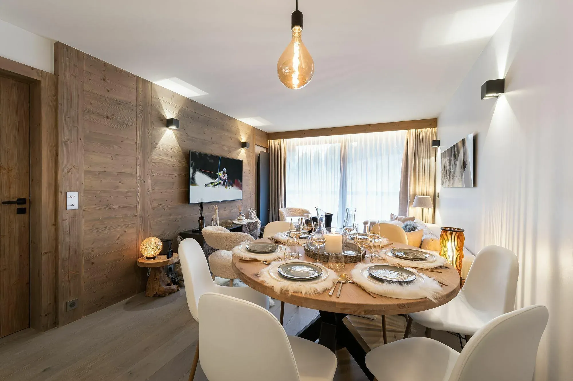 Dining area with round table, four white chairs and wood-panelled wall