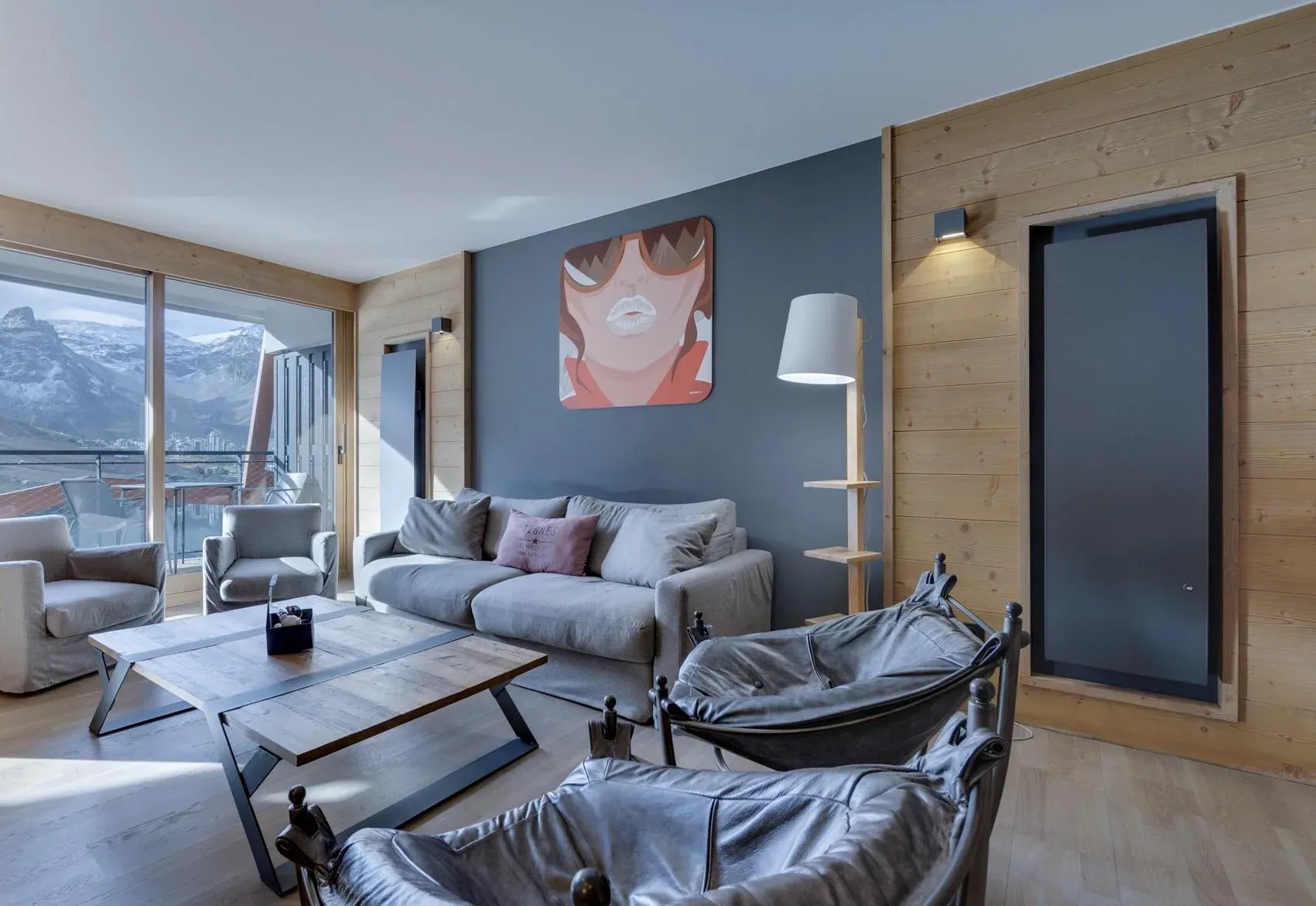 Living room with grey sofa, leather armchairs and balcony doors facing the mountains