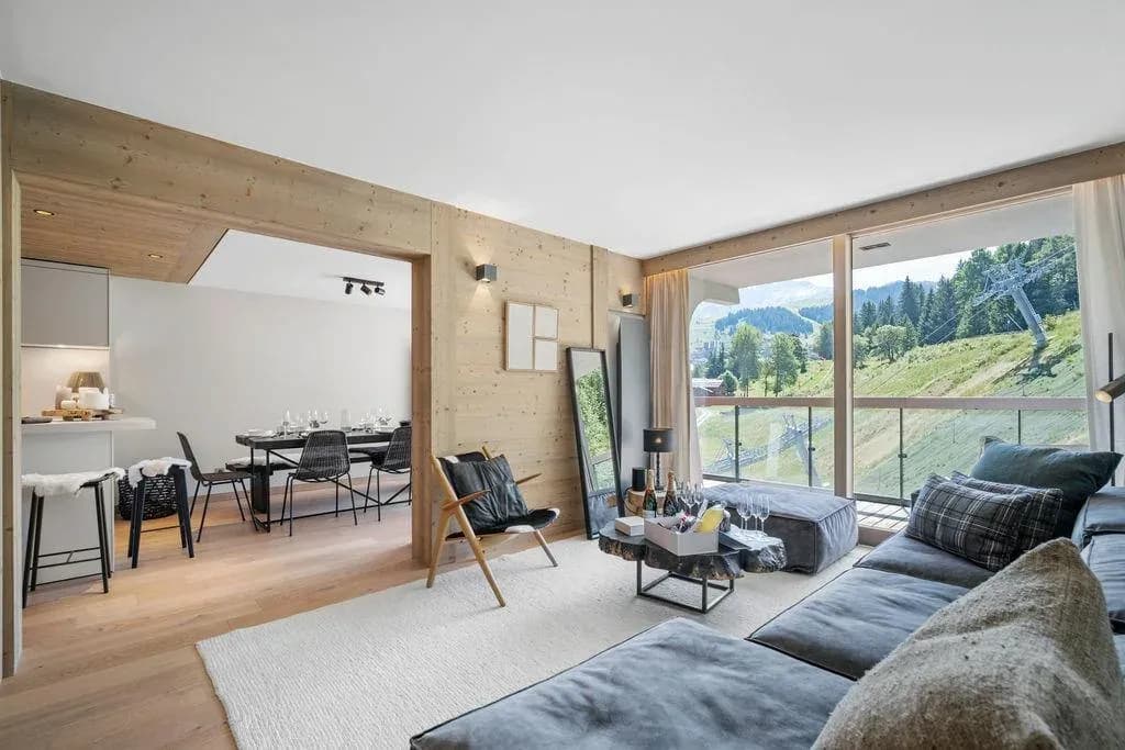 Living room with grey modular sofa, wood-panelled walls and balcony doors facing the slopes