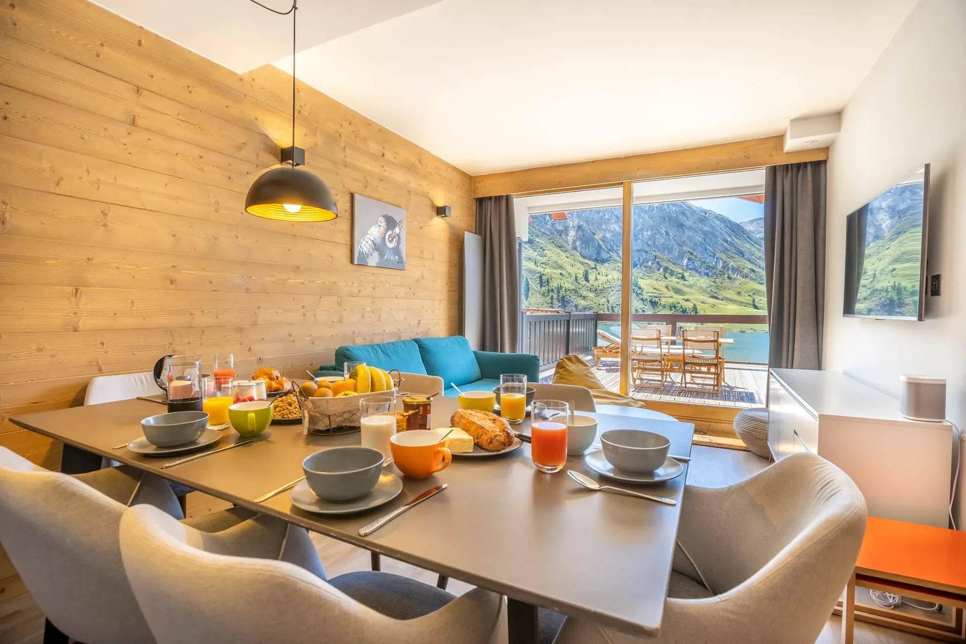 Dining table set for breakfast with six chairs and mountain view through glass doors