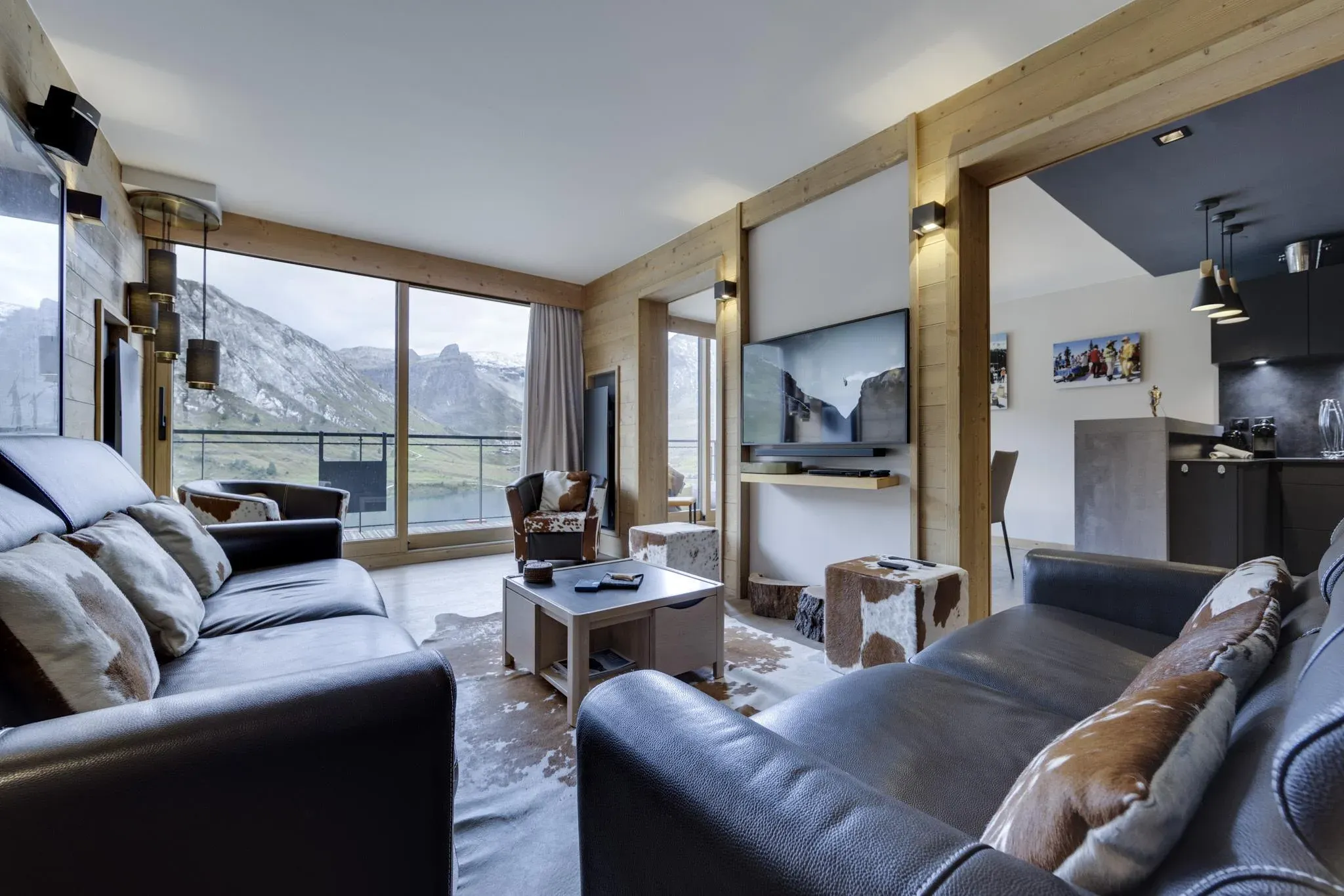 Living room with two leather sofas, wall-mounted TV and floor-to-ceiling mountain views