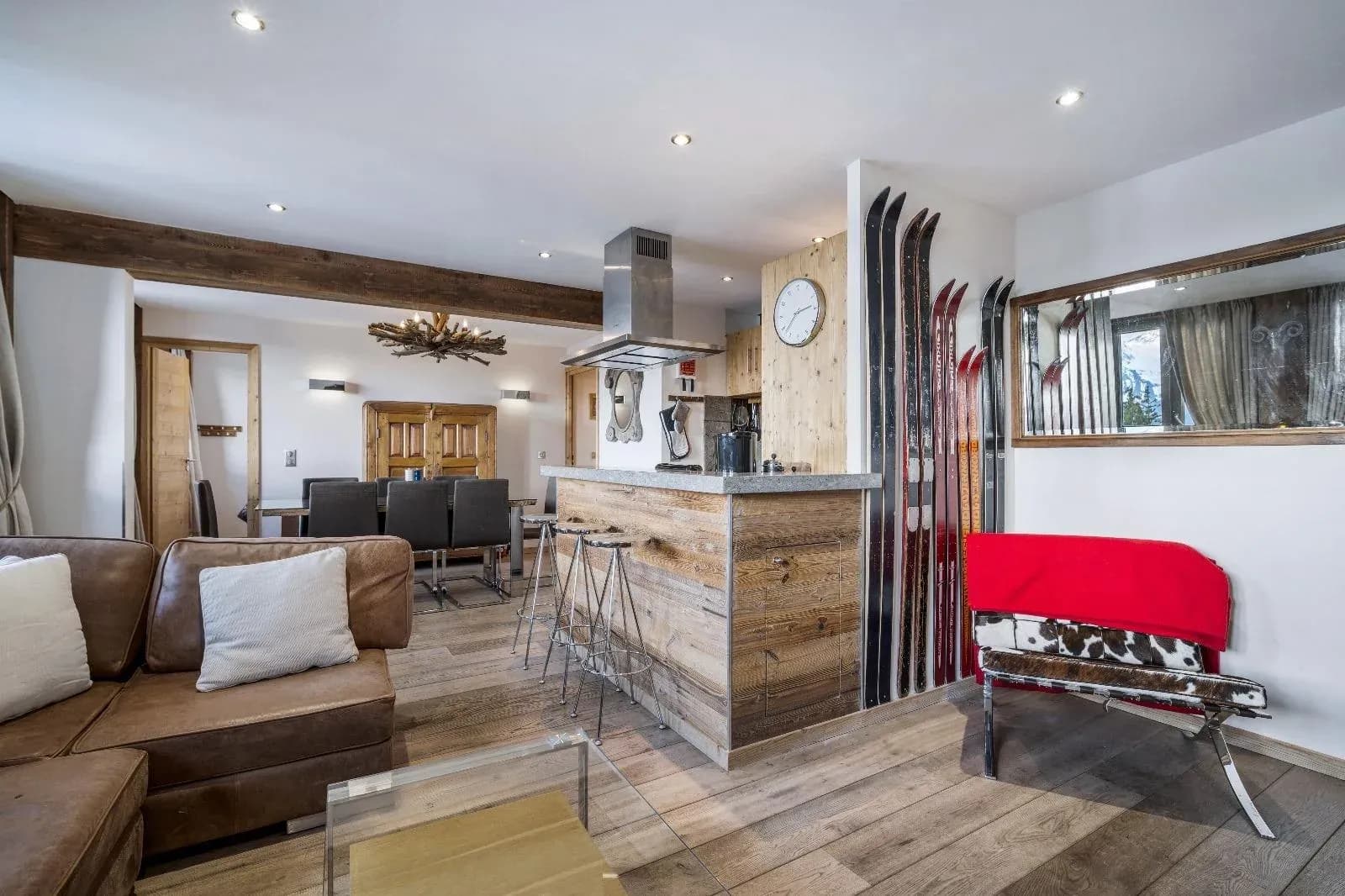 Open-plan living area with leather sofa, breakfast bar with three stools and skis on the wall