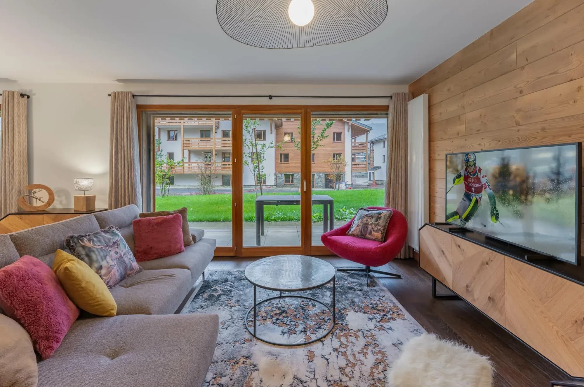 Living room with grey corner sofa, red armchair and glass doors to the terrace