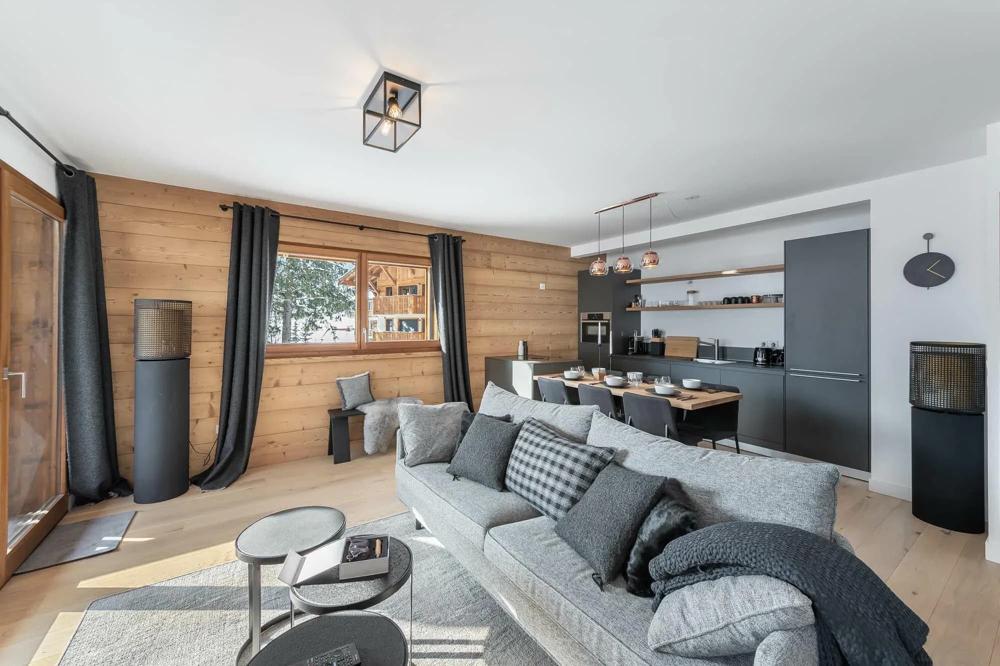 Living area with grey sofa, wood-panelled wall and open kitchen behind