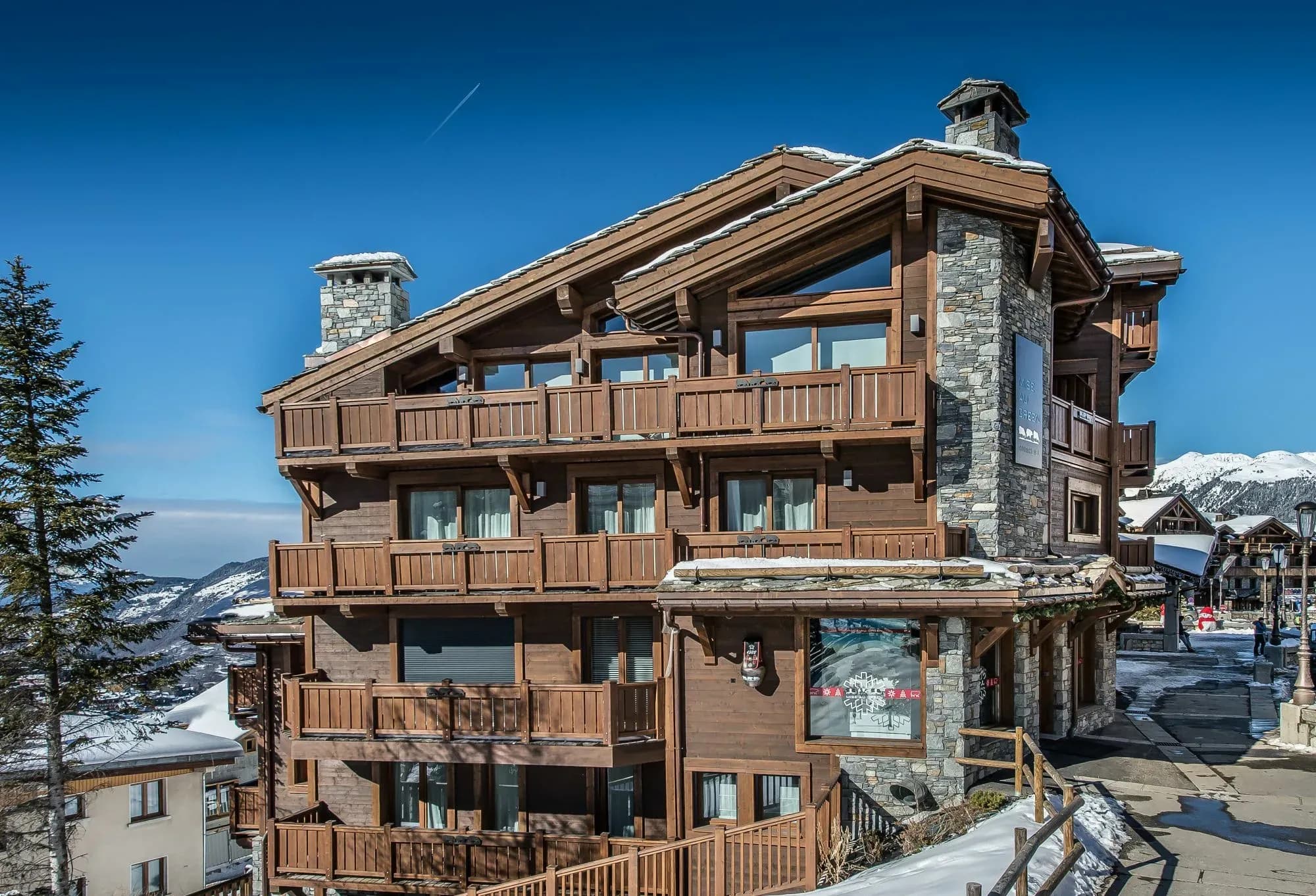 Wood and stone chalet building with balconies on each floor and snowy street