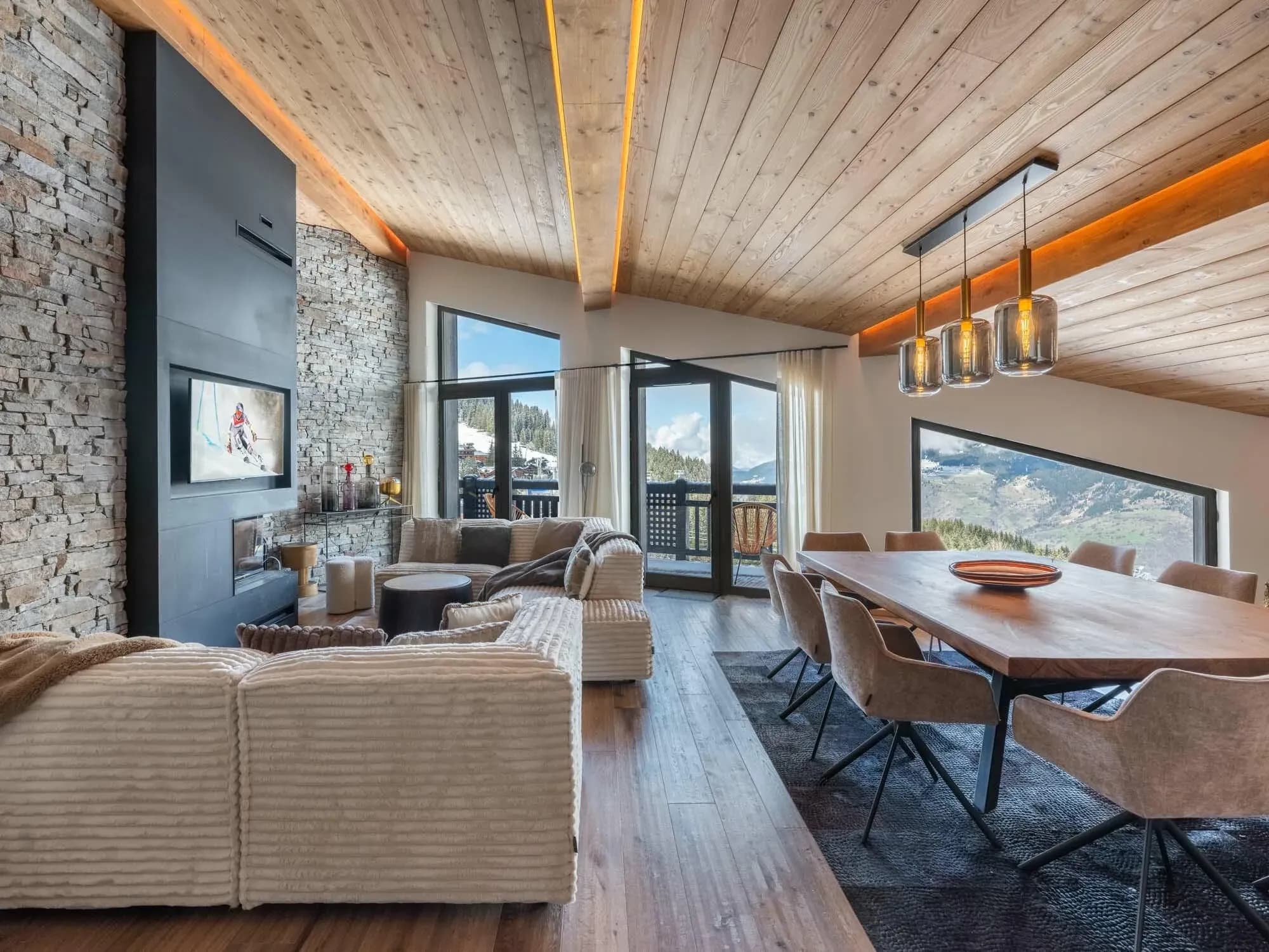 Open-plan living and dining area with corner sofa, fireplace and mountain views