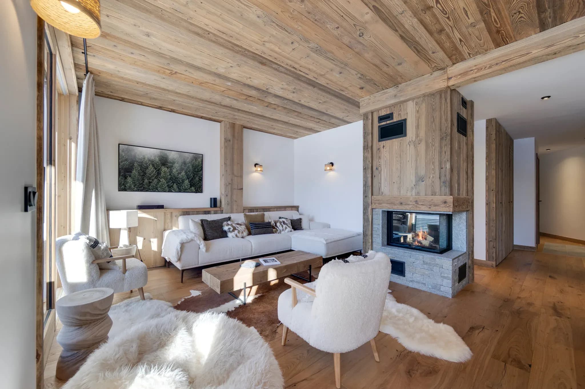 Living room with corner sofa, sheepskin armchairs and glass-fronted wood fireplace