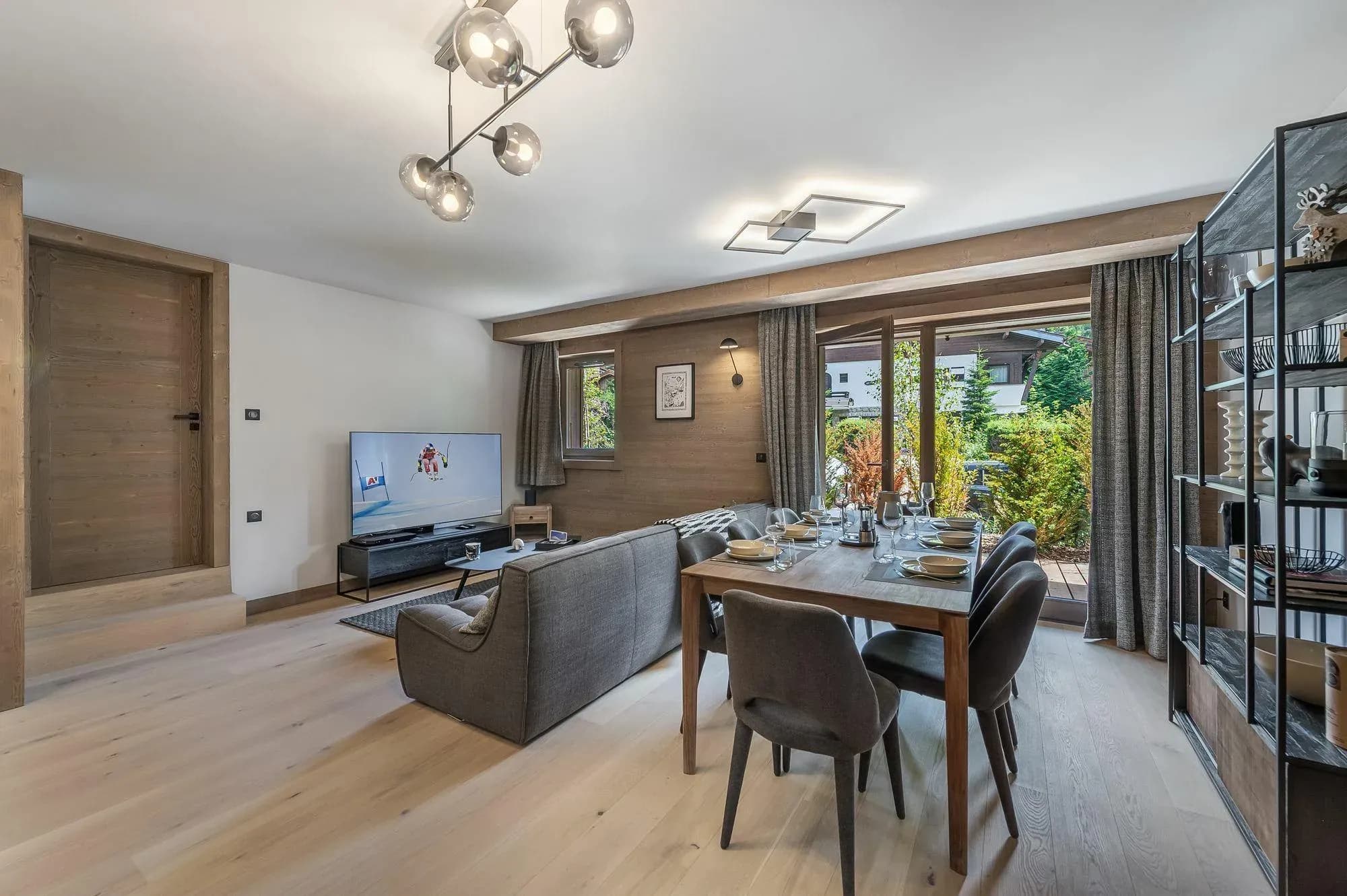Open-plan lounge with grey sofa, TV and dining table beside garden doors