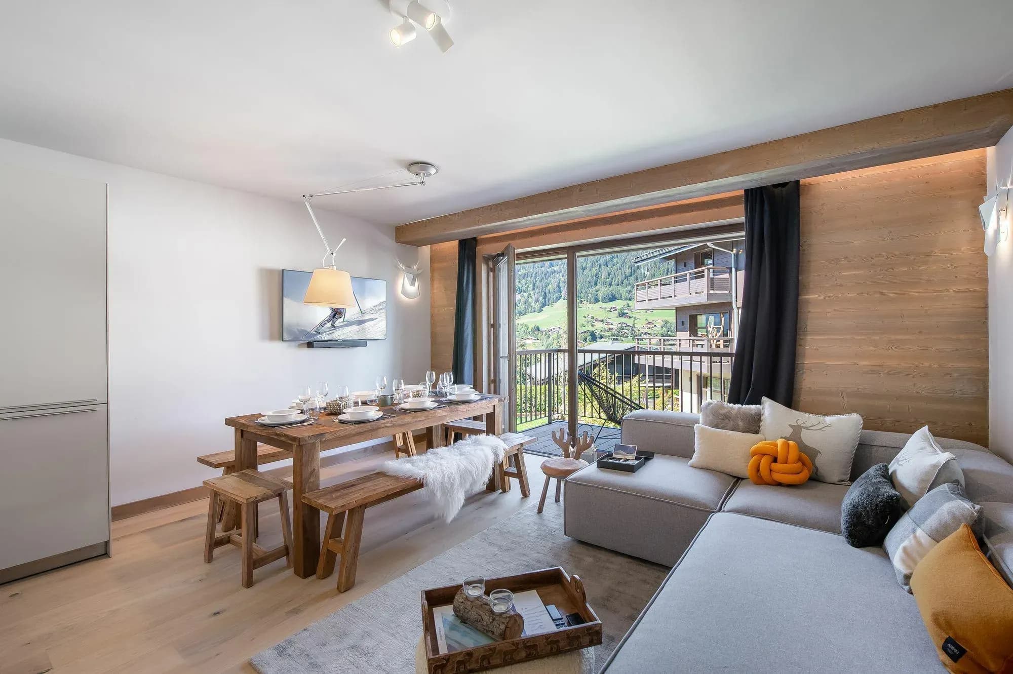 Dining area with wooden table and benches beside sofa and balcony doors