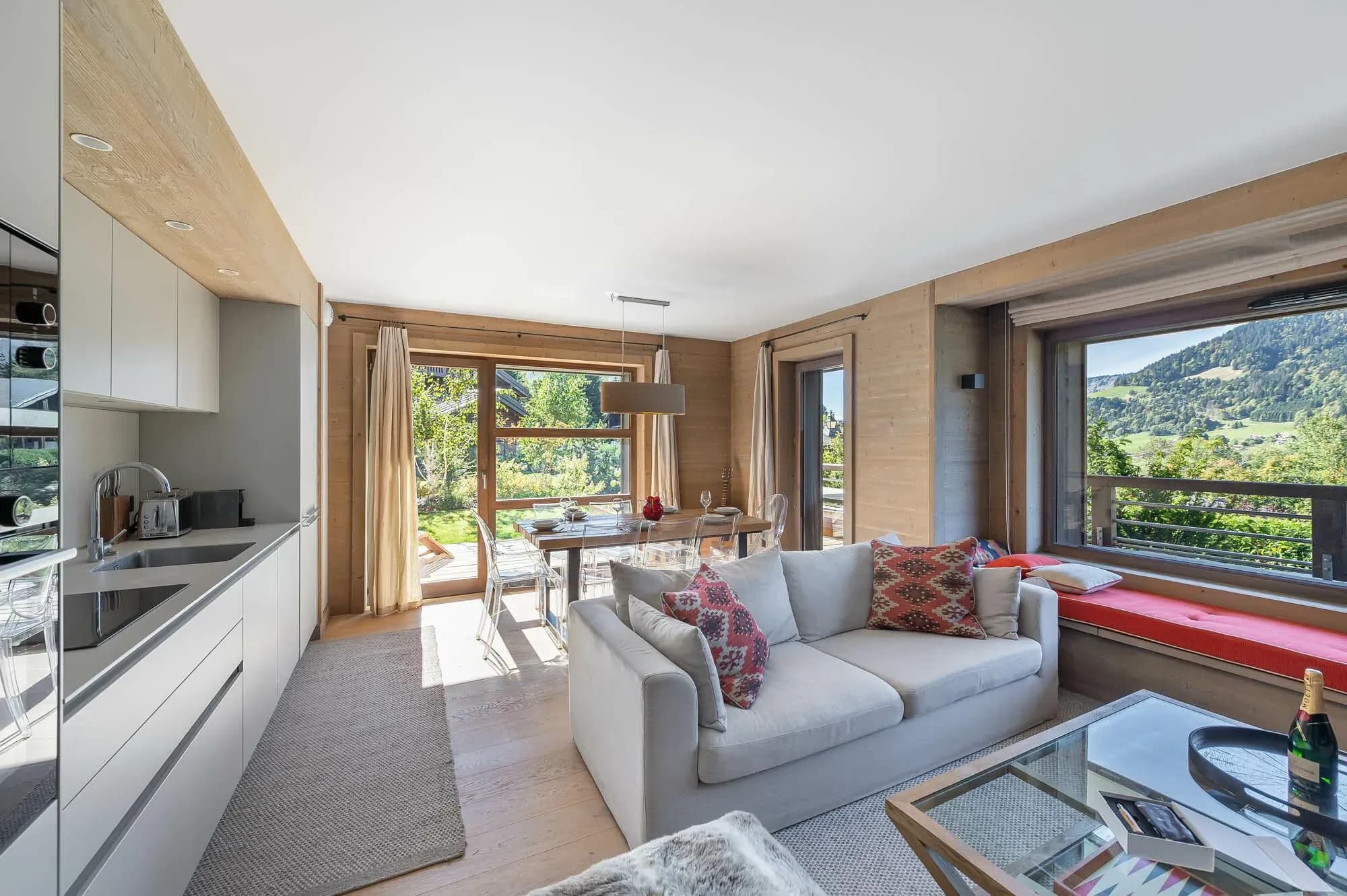 Open-plan living area with grey sofa, window seat and mountain view