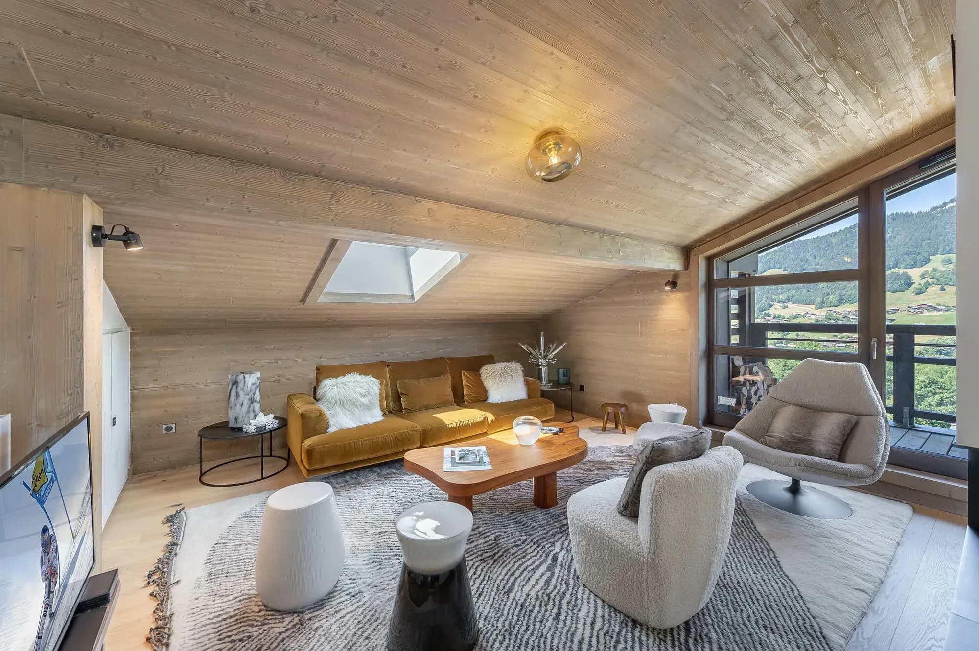 TV lounge with mustard sofa, armchairs and sloping wood ceiling beside a balcony window