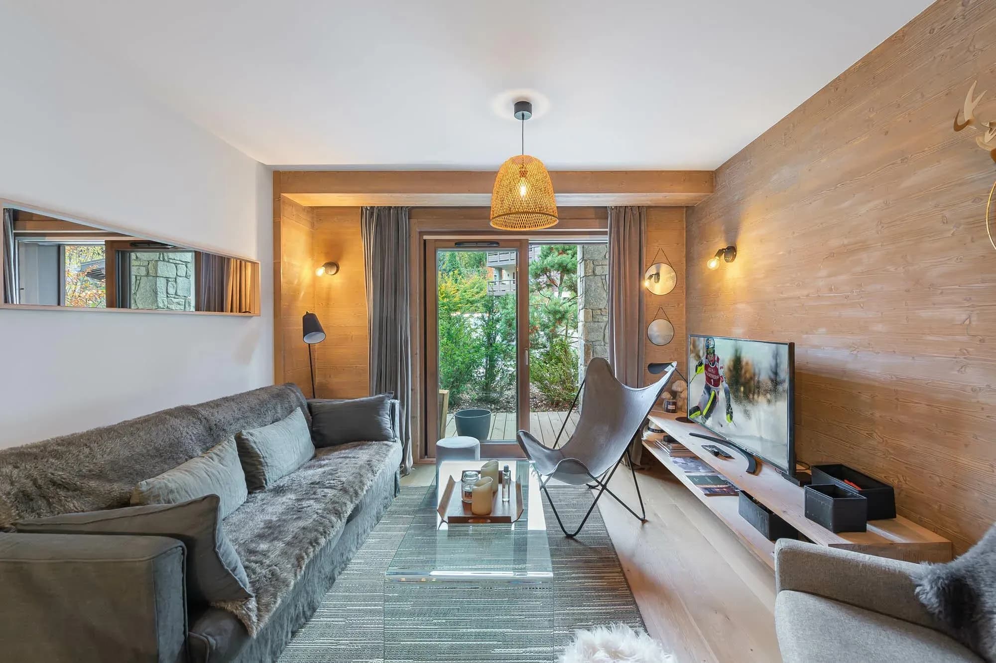 Living room with grey sofa, butterfly chair and glass coffee table by patio doors